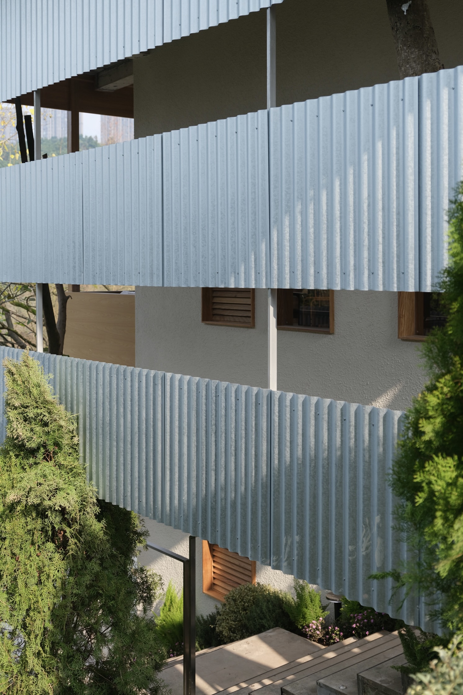 Stacked facade with corrugated metal panels and horizontal strip windows surrounded by trees