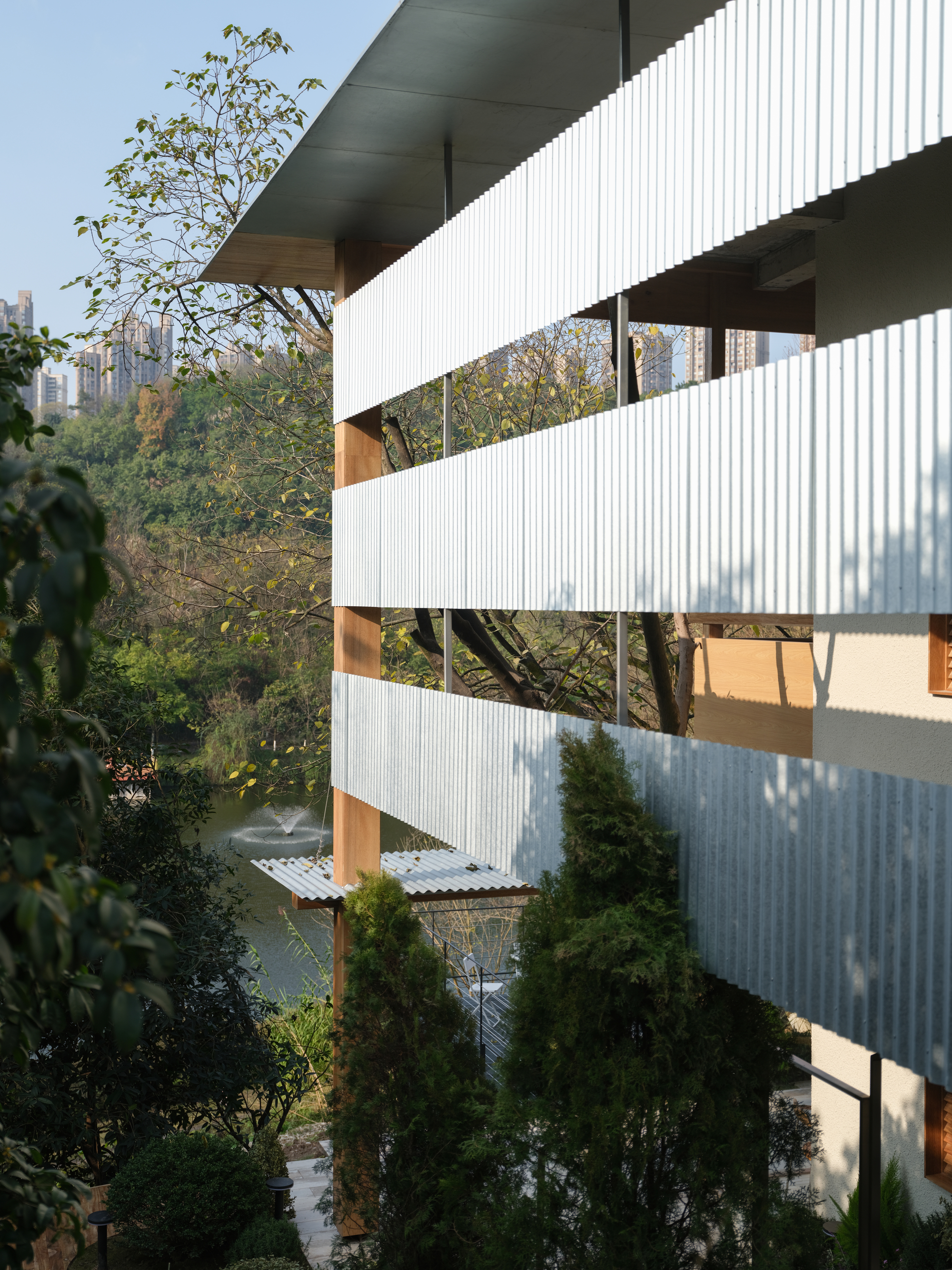 Layered facade with alternating corrugated metal screens and recessed openings in afternoon light
