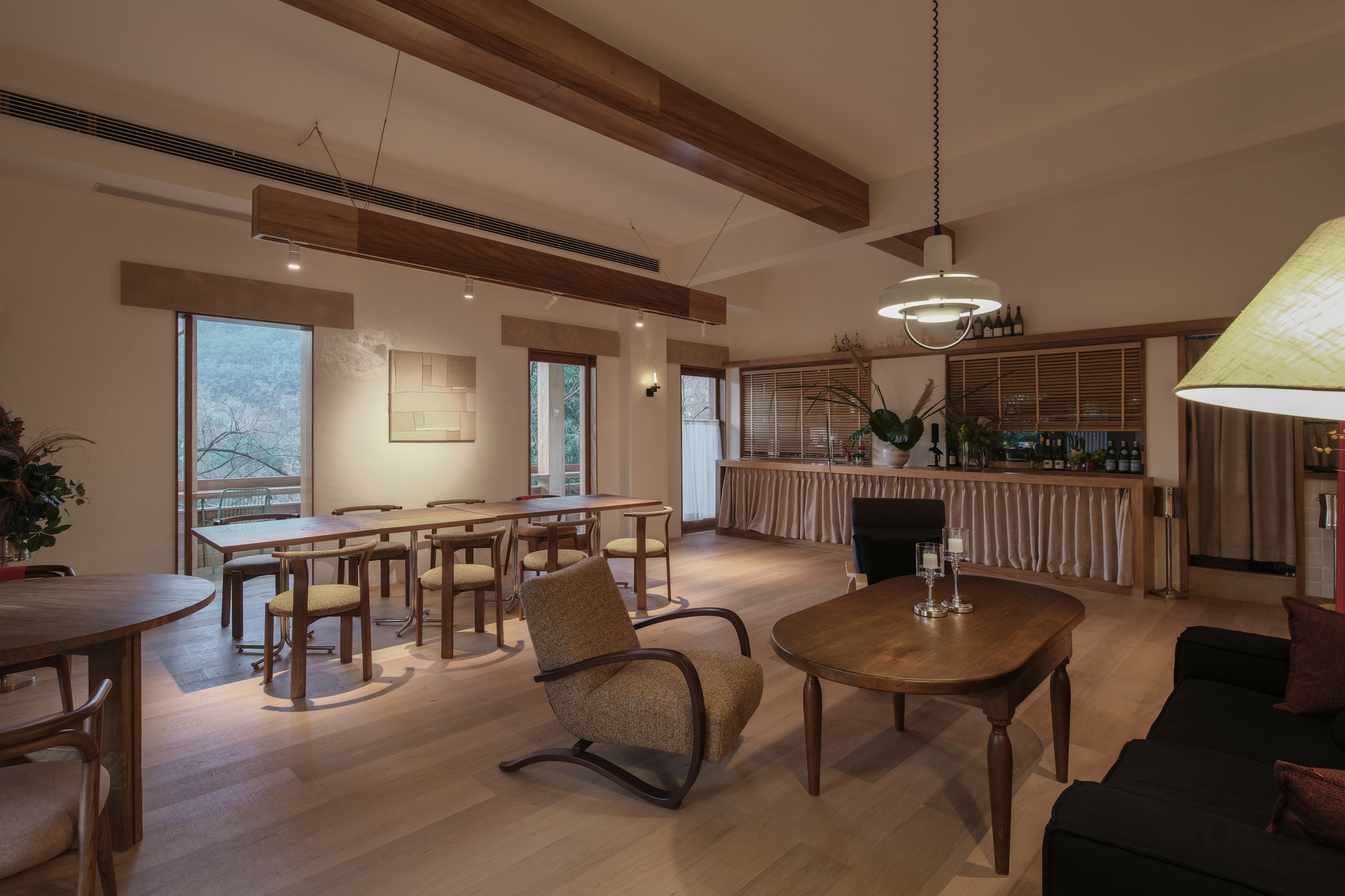 Open dining and lounge space with exposed timber beams and a bar counter under evening lighting