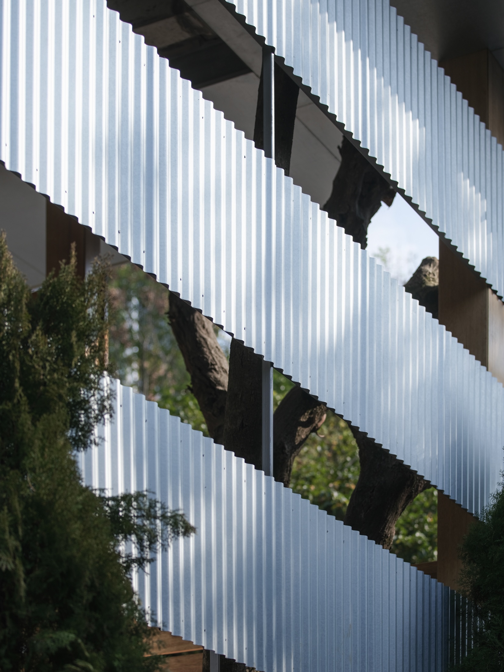 Vertical translucent panel screen with diagonal cutouts revealing trees and structure behind