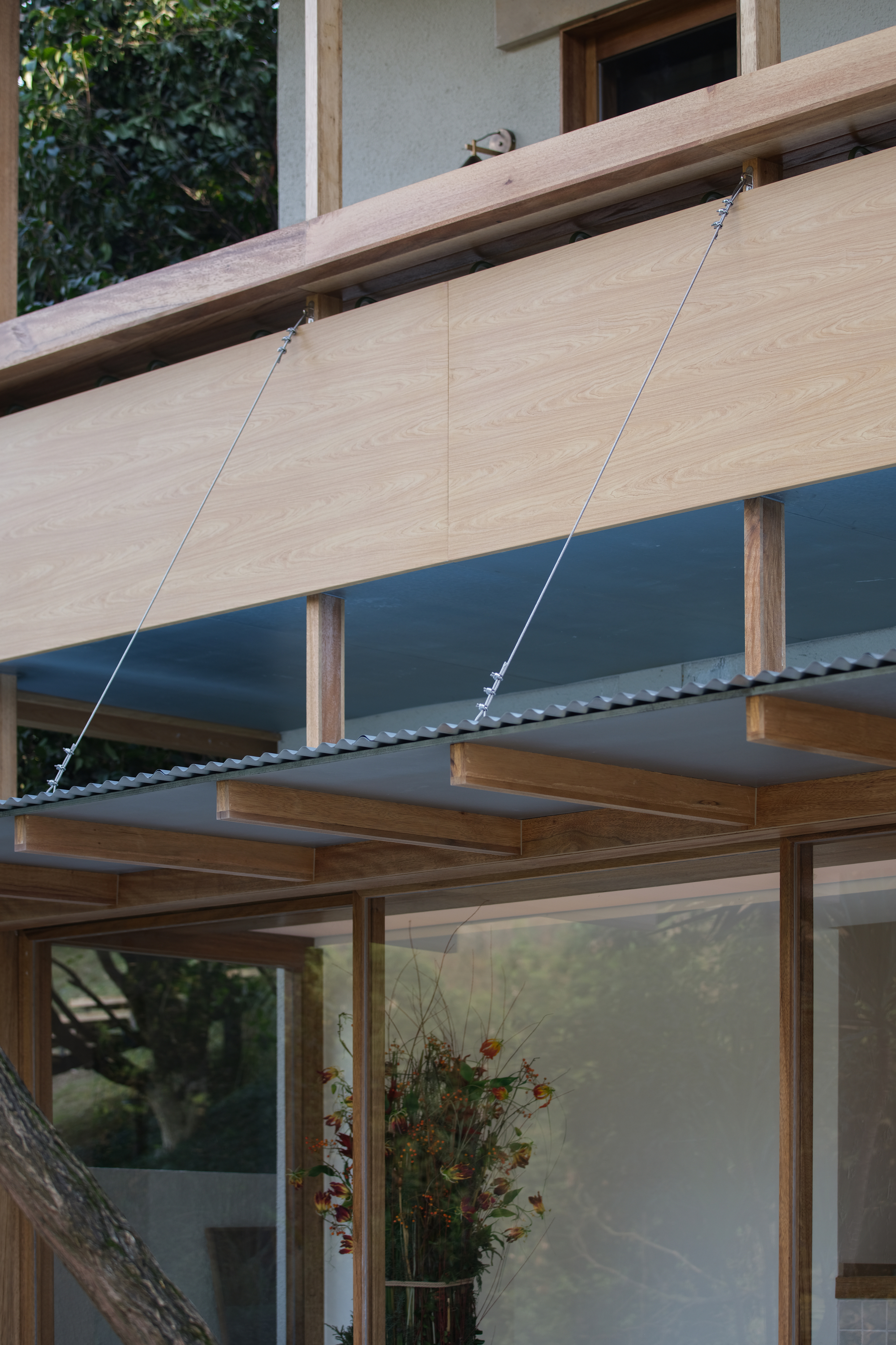 Timber overhang with cable suspension system above glazed opening and timber frame below