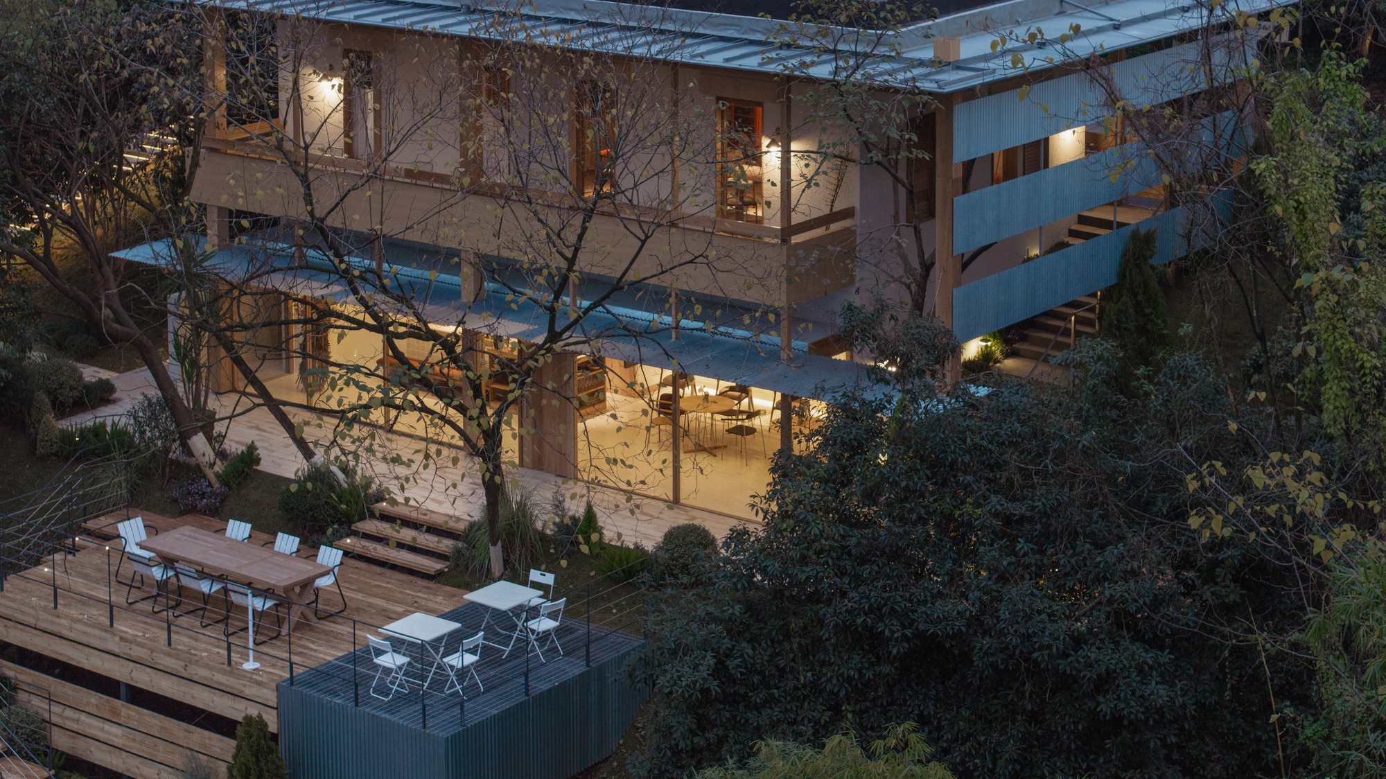 Three-level residence with corrugated roof and outdoor terrace lit at twilight