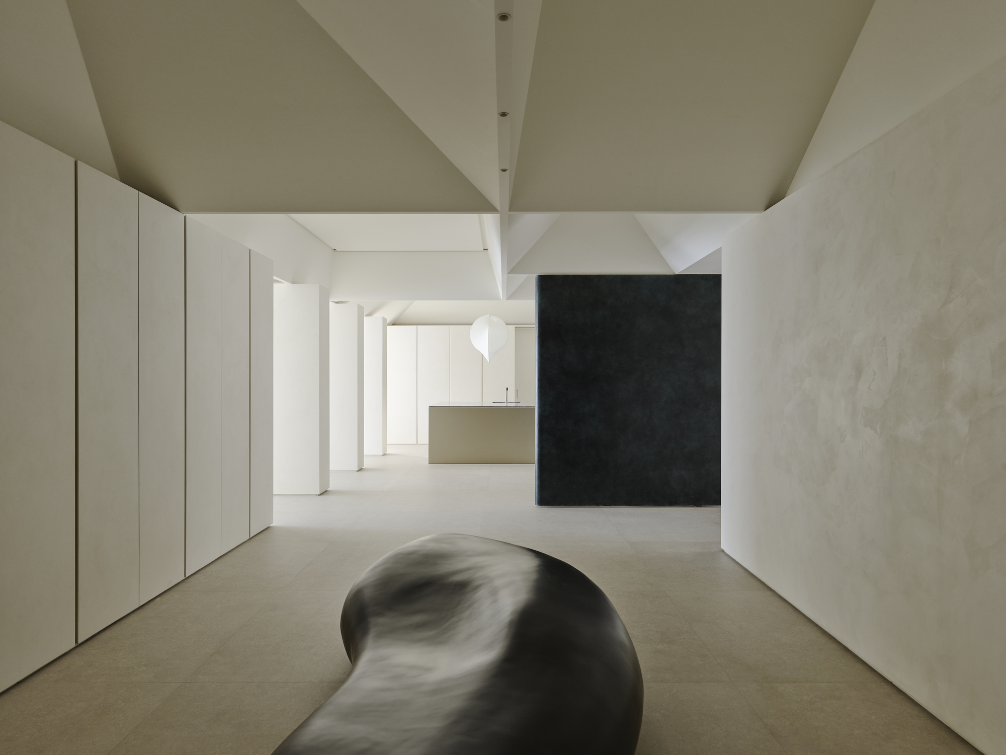 Open interior with curved black sculpture on the floor beneath angular white ceiling planes and textured columns