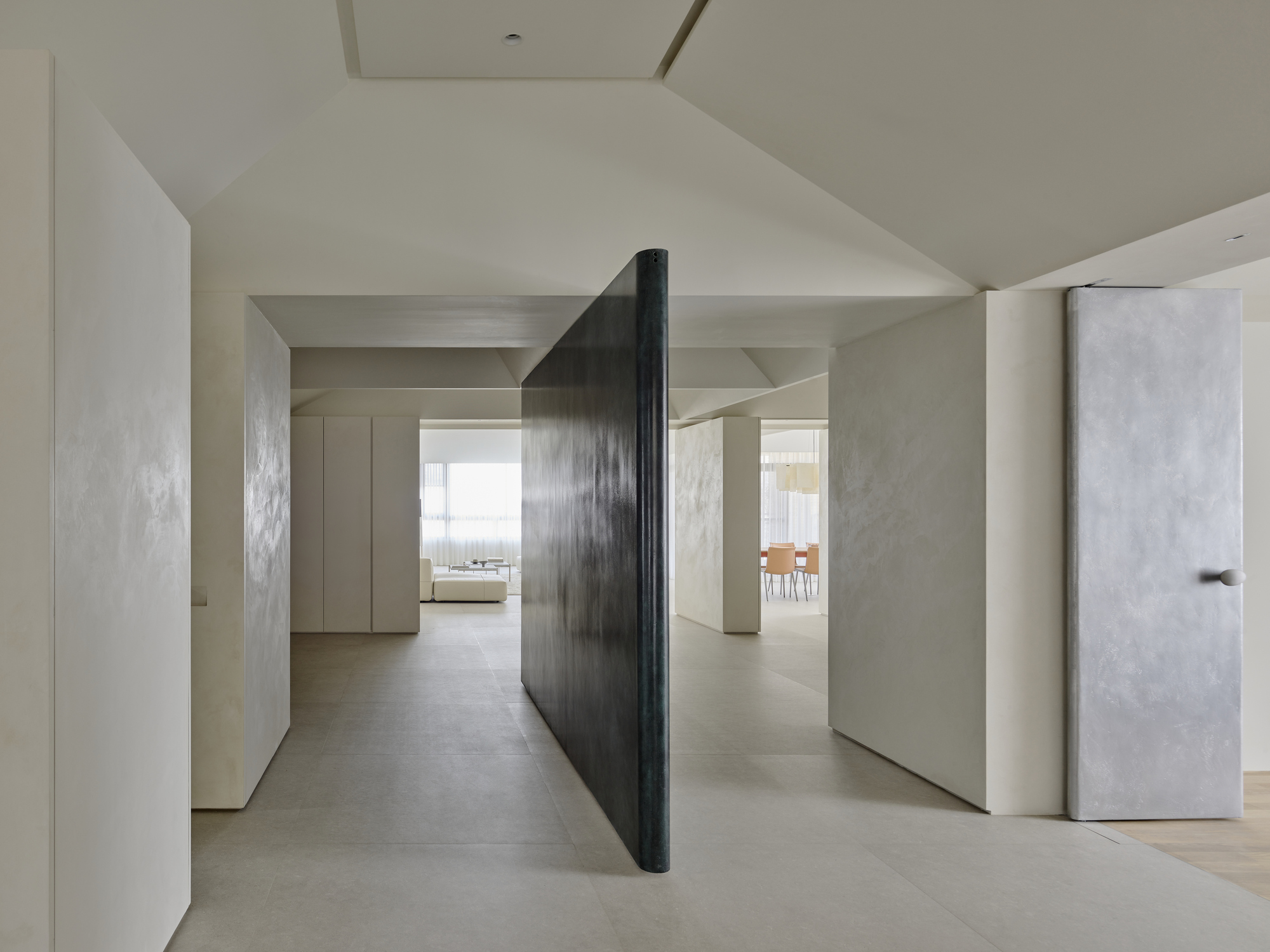 Pivoting dark metal partition between pale plaster walls with view through to daylit rooms beyond