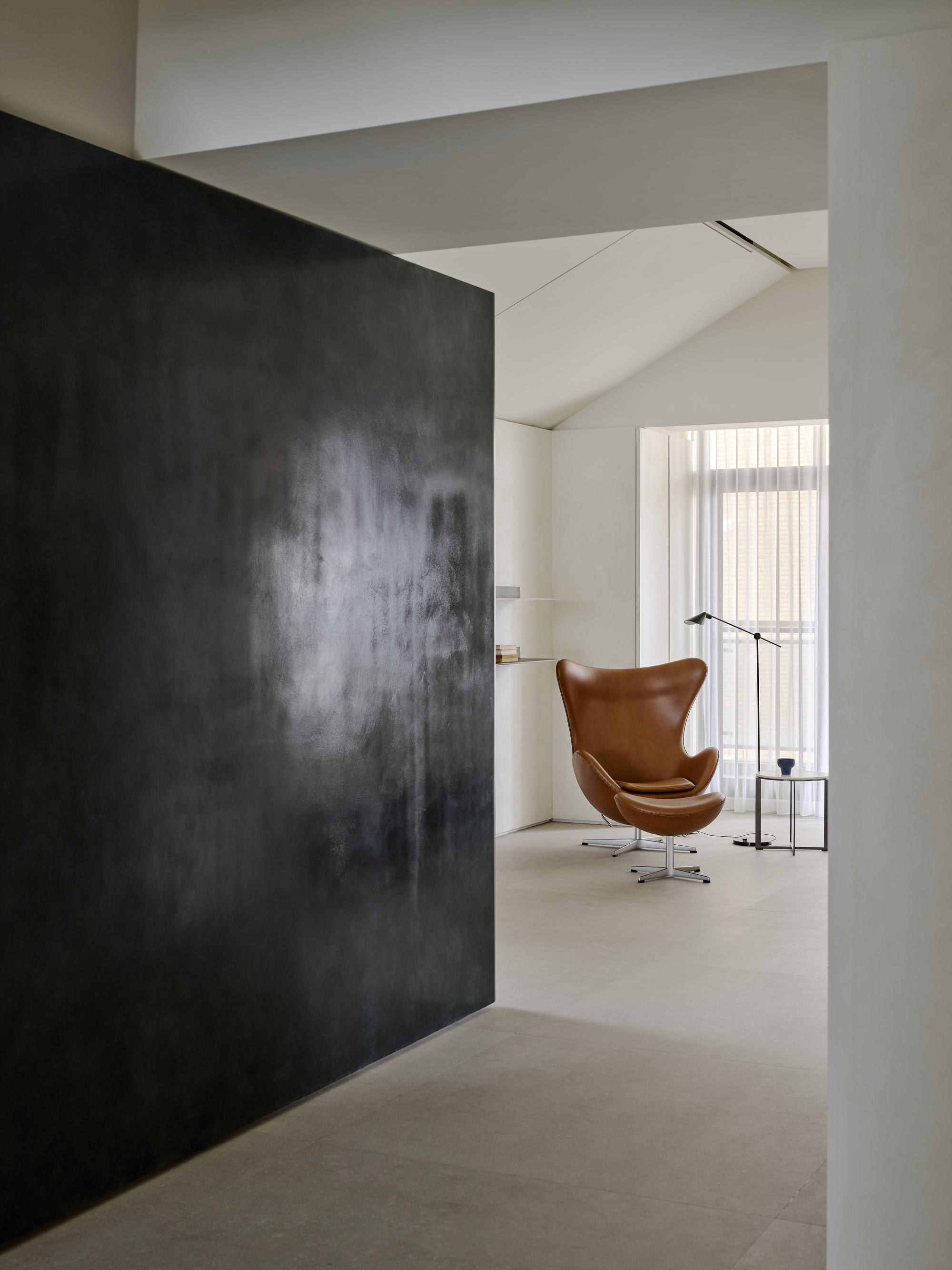 Dark textured wall panel framing a tan leather chair beside a floor lamp and window