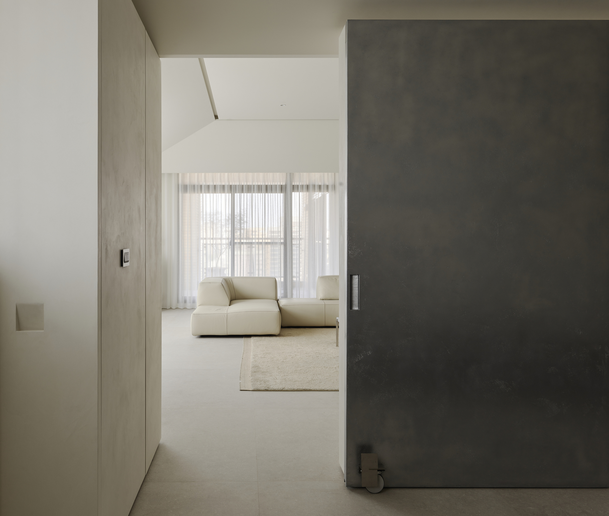 Narrow corridor framed by dark sliding panel opening to sitting area with sheer curtains