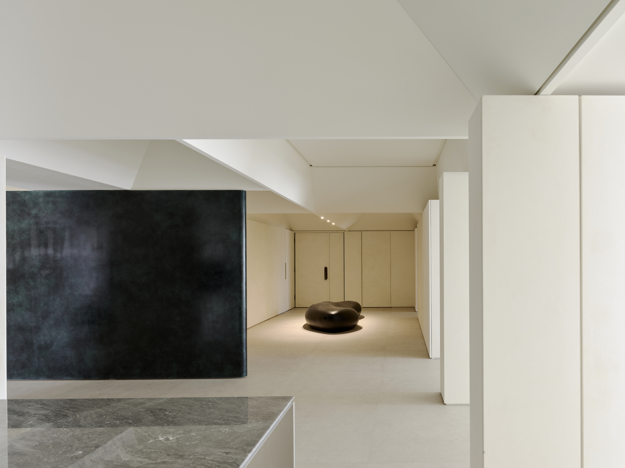 Open interior gallery with dark feature wall and pale wood cabinetry beneath angular ceiling planes