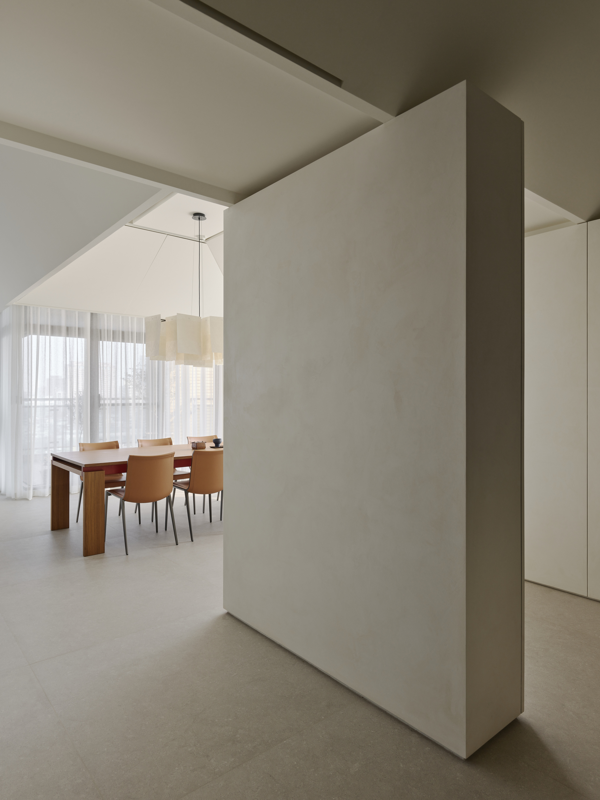 Freestanding partition wall separating spaces with dining area visible through sheer curtained windows beyond