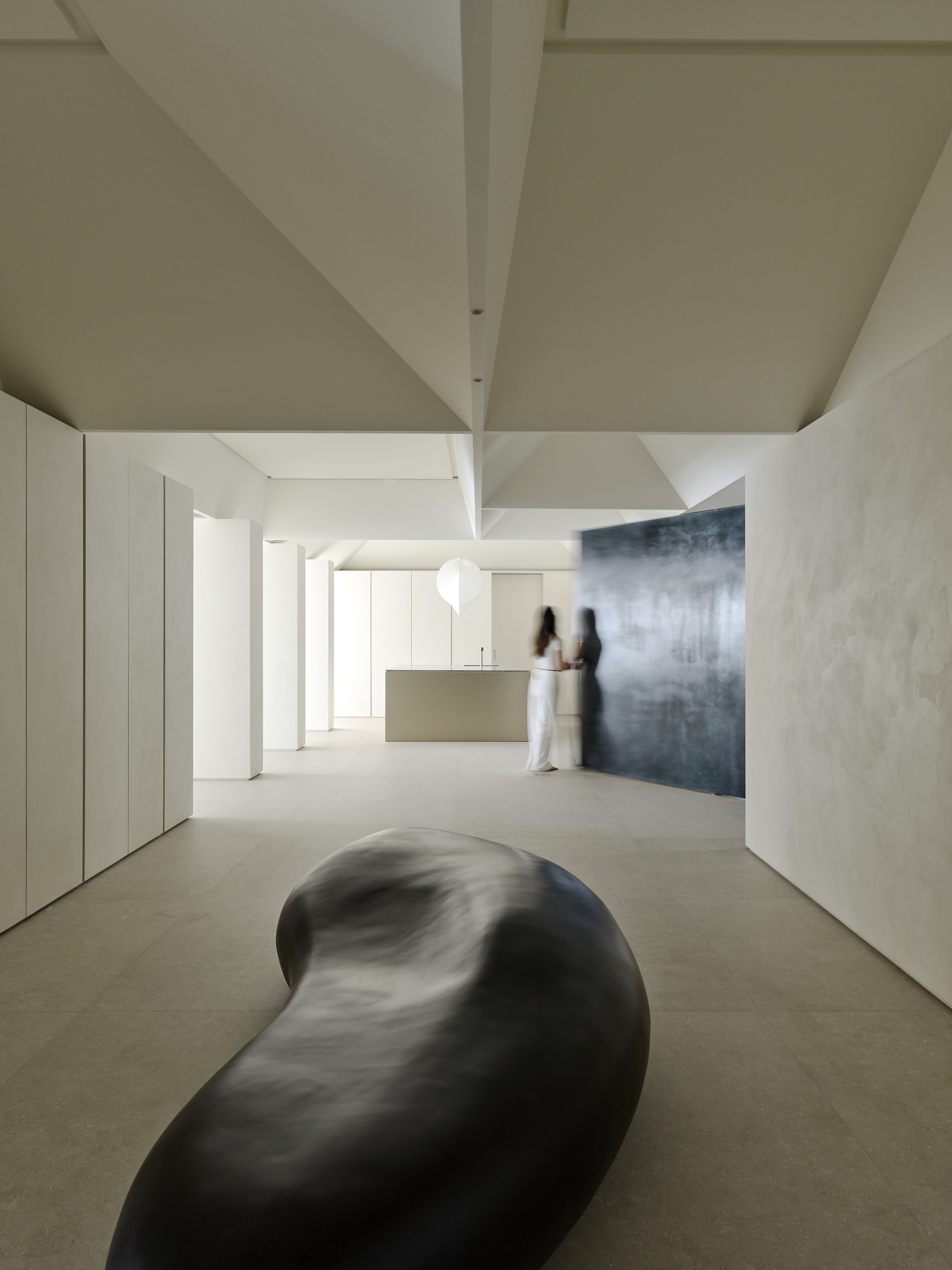 Open living space with sculptural black form on floor and two figures near kitchen island