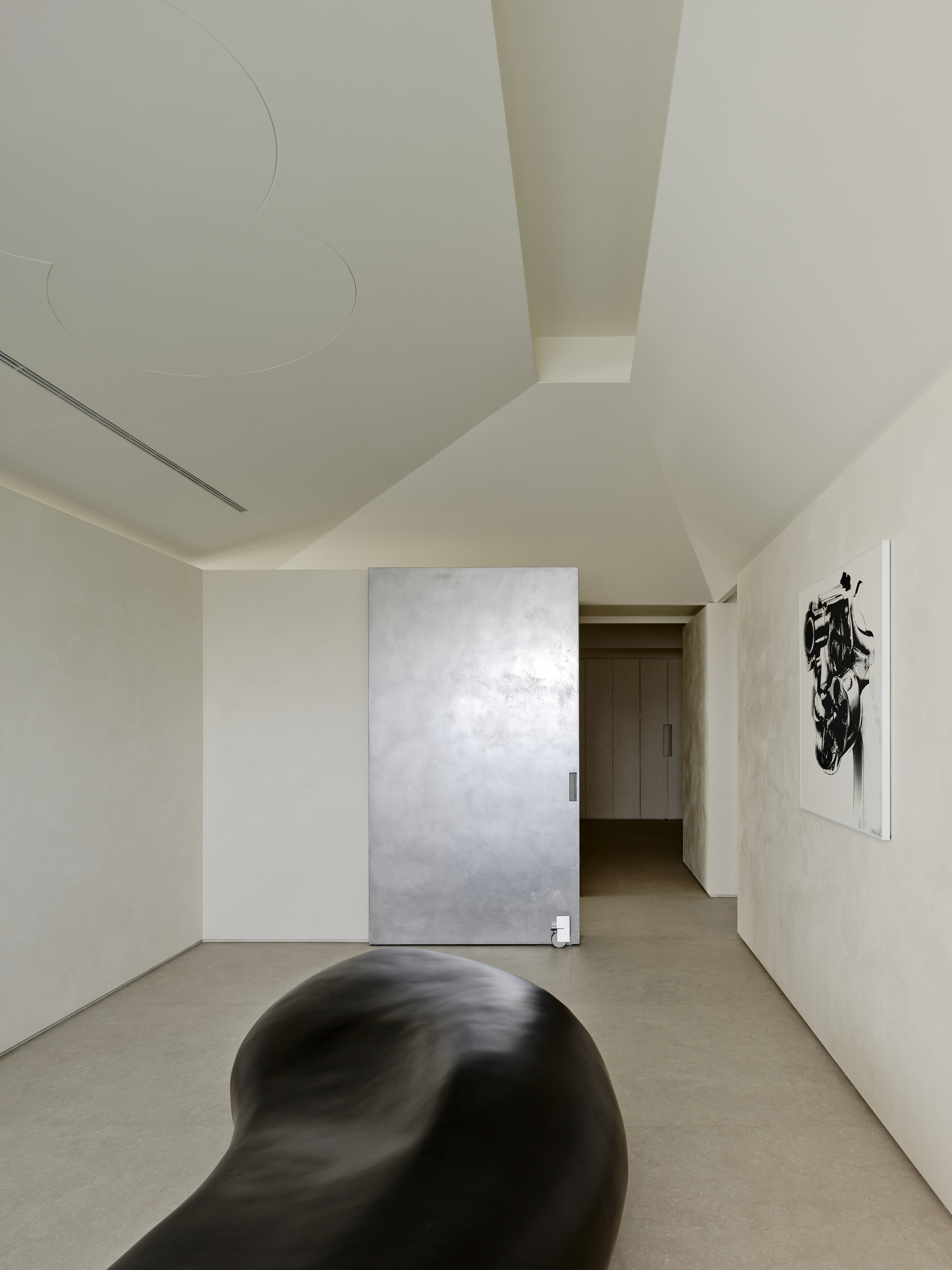 Hallway with sliding metallic door panel and artwork beside organic black sculpture on concrete floor