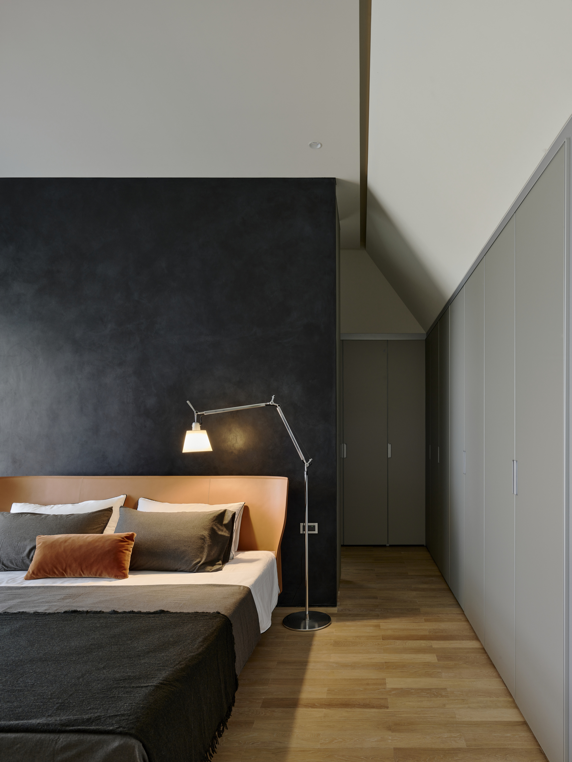 Bedroom with articulated task lamp beside bed against charcoal accent wall and timber flooring
