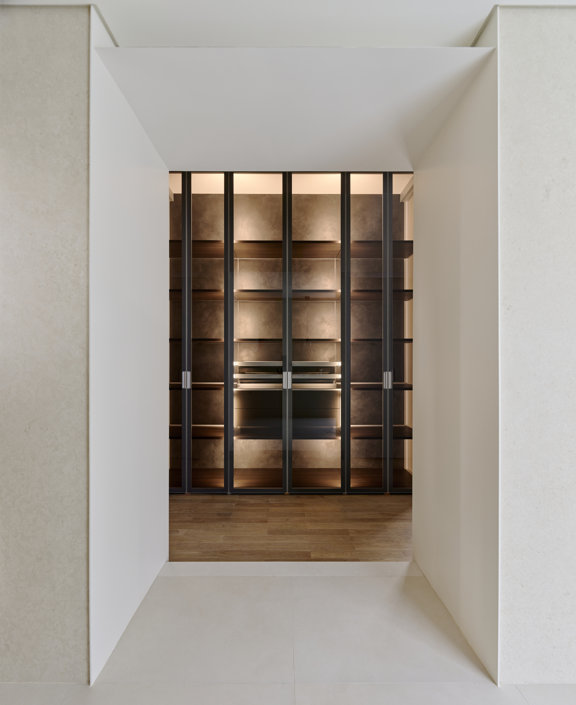 View through a white portal to illuminated glass and metal shelving units on wooden flooring