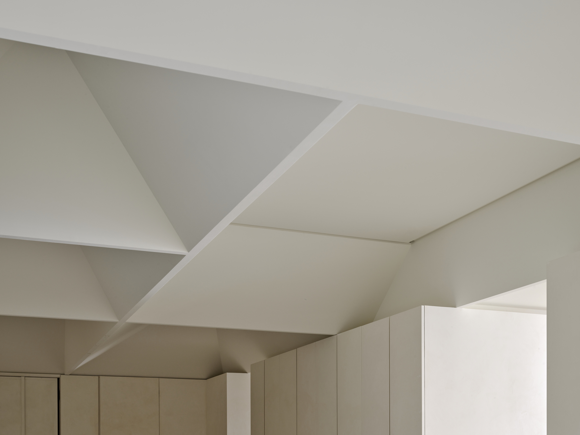 Faceted white ceiling with geometric triangular planes above pale cabinetry