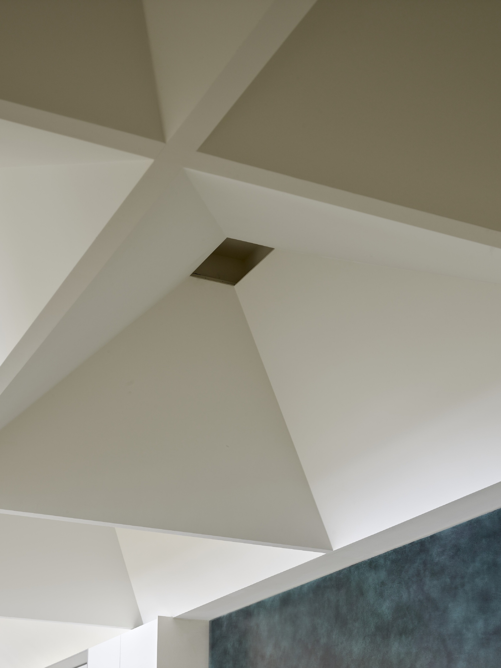 Angular white ceiling planes with small recessed vent opening above textured wall surface