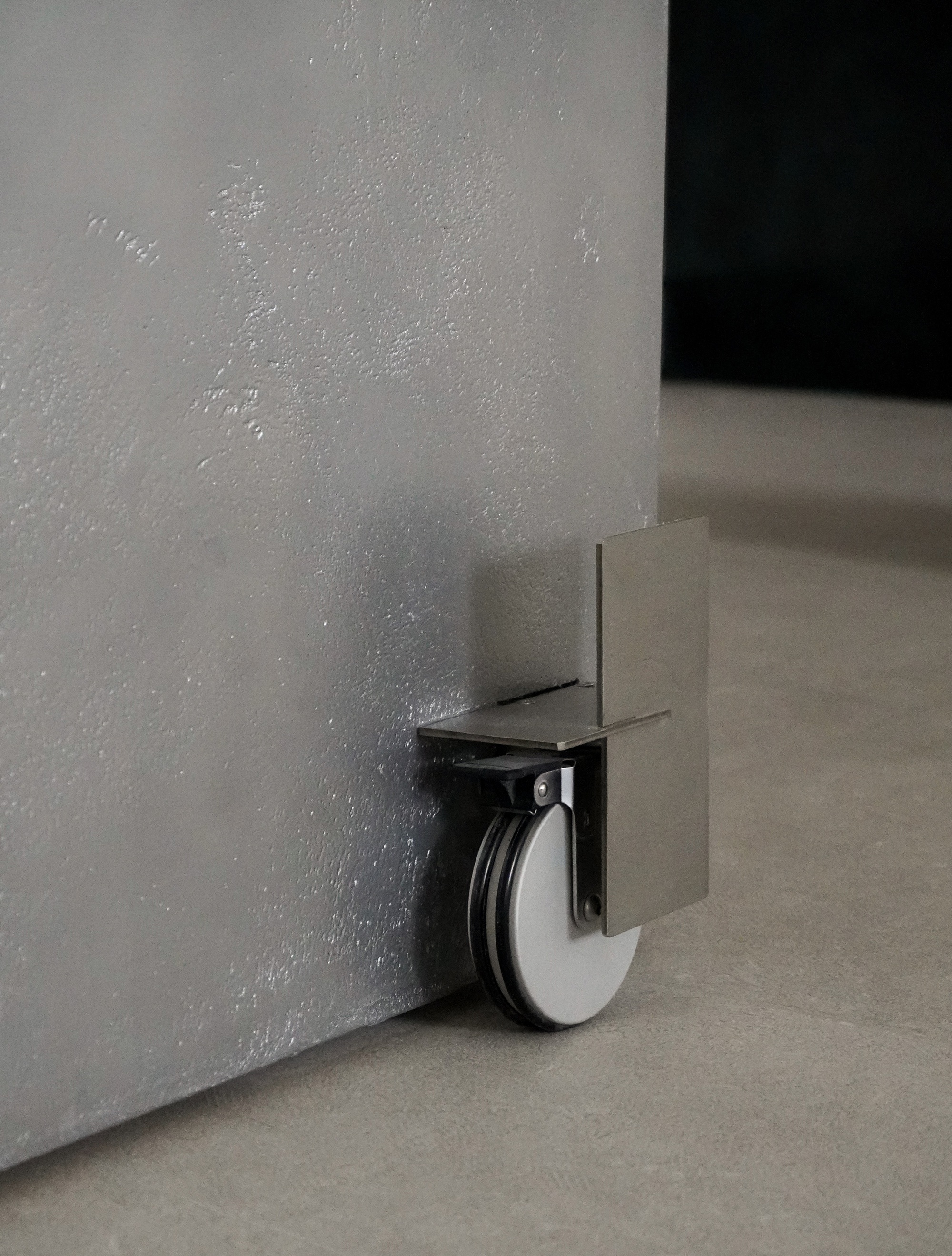 Close-up of metal castor wheel mounted beneath textured grey partition panel
