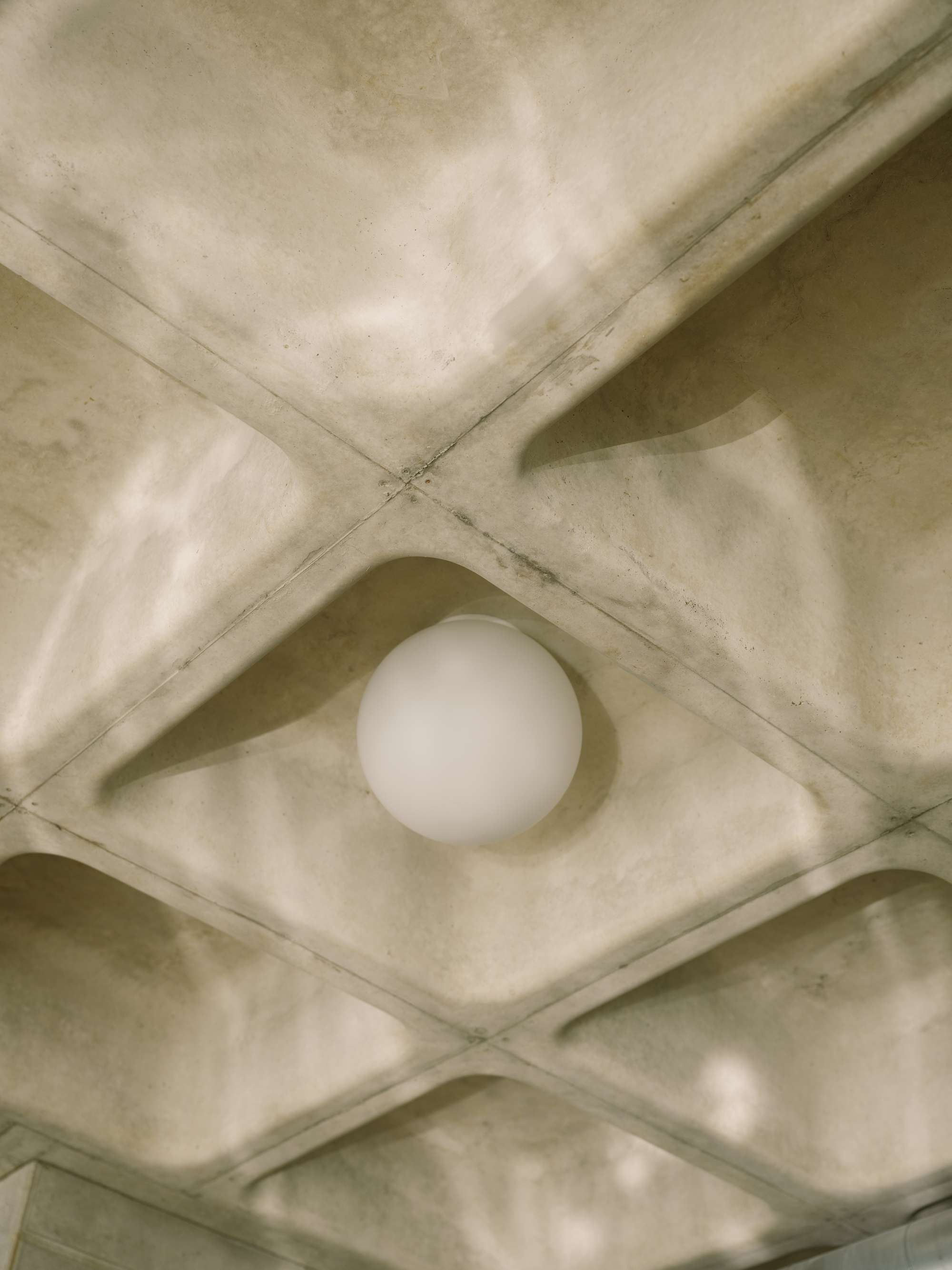 Single globe light fixture nested within a diamond-shaped concrete waffle ceiling coffers
