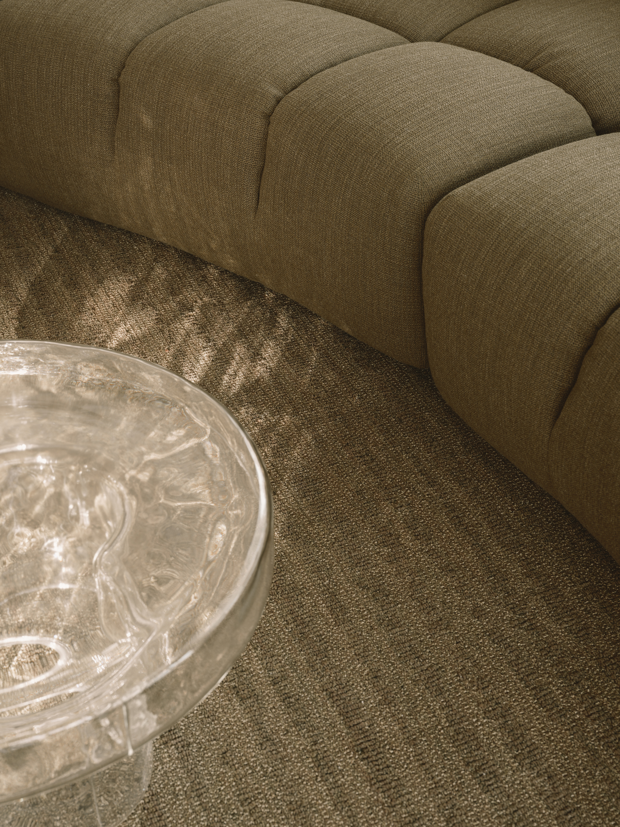 Detail of curved upholstered sofa modules beside a clear resin coffee table on textured carpet