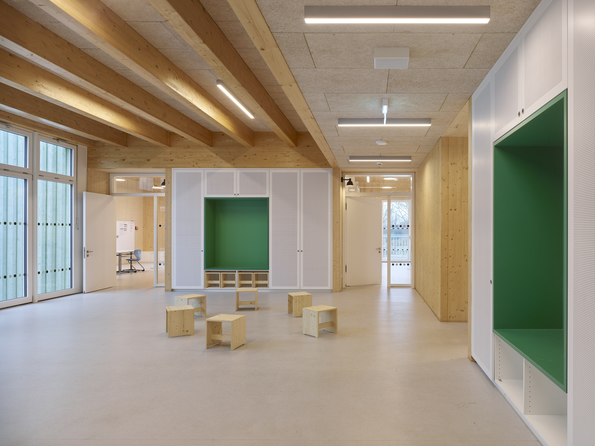 Interior classroom with exposed timber beams, plywood partitions with green alcoves, and light wood benches