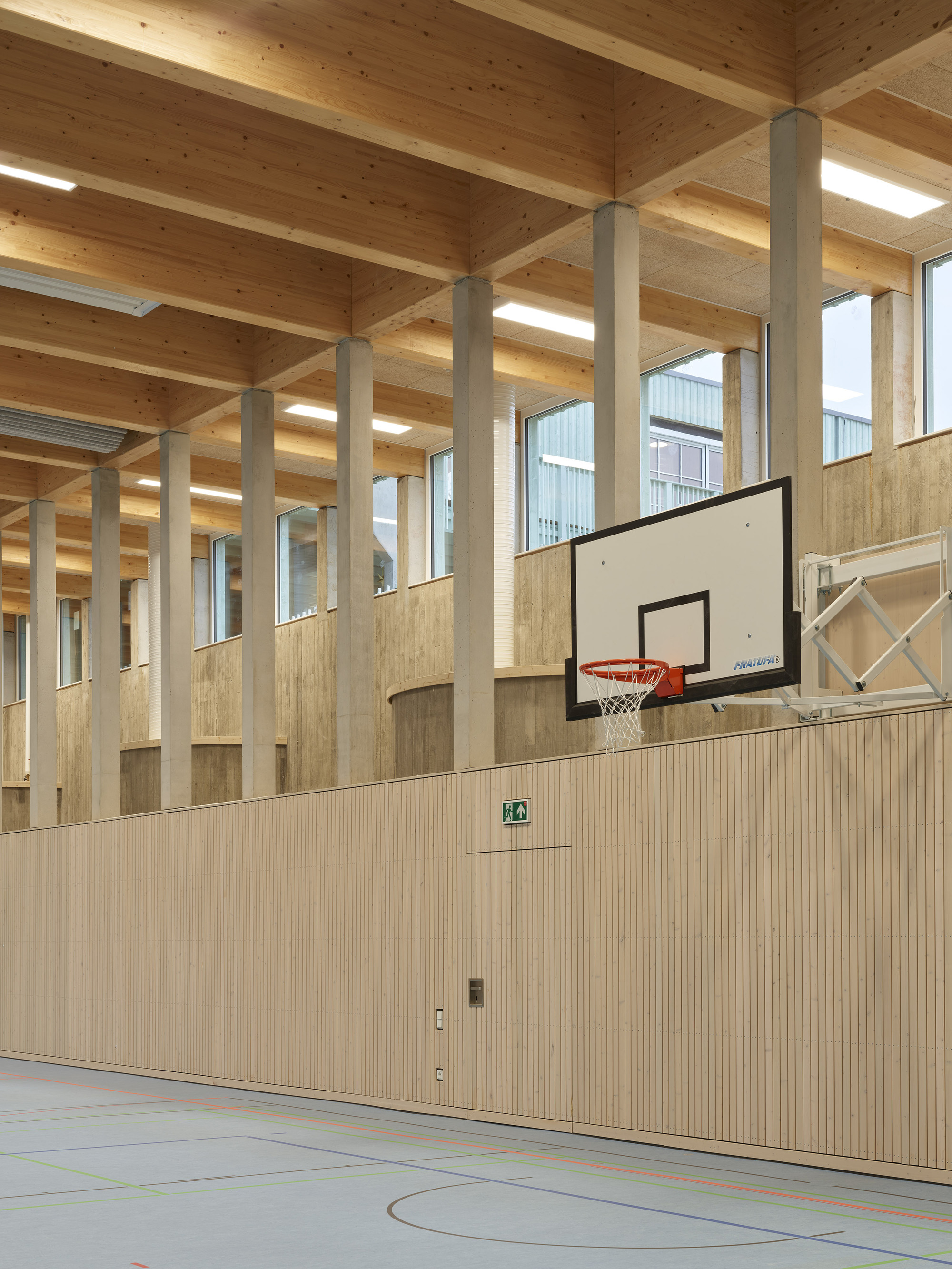 Gymnasium interior with basketball hoop, light wood paneled walls, and exposed timber post and beam ceiling