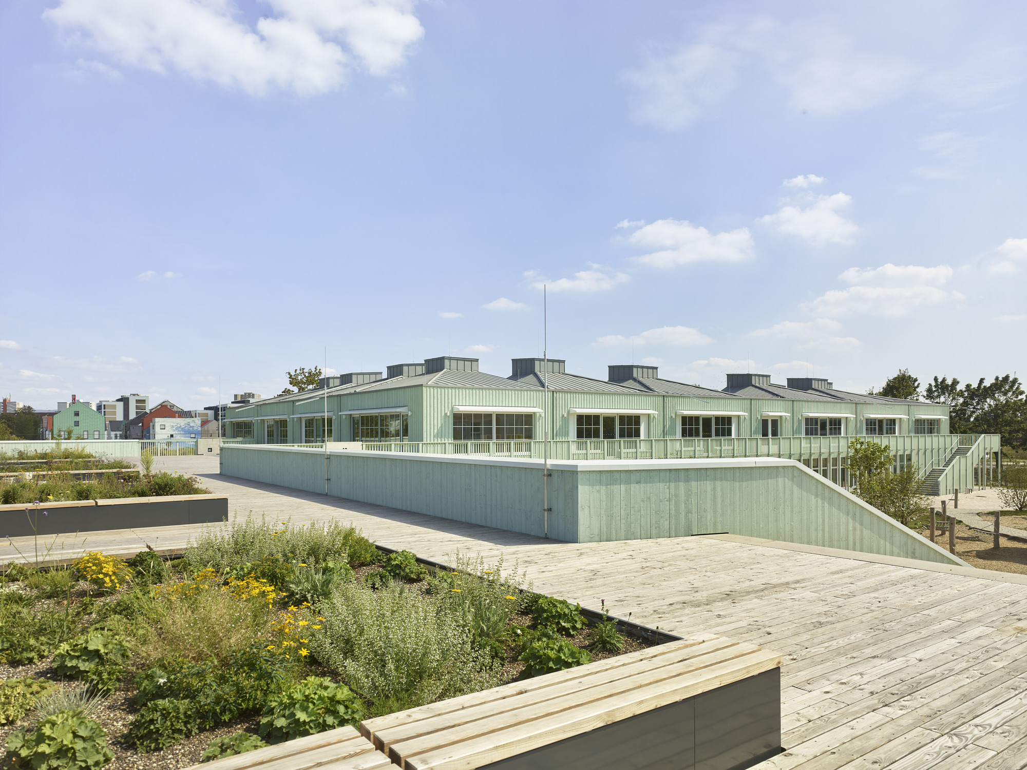 Rooftop garden with planted beds and pale green corrugated metal facade under a partly cloudy sky