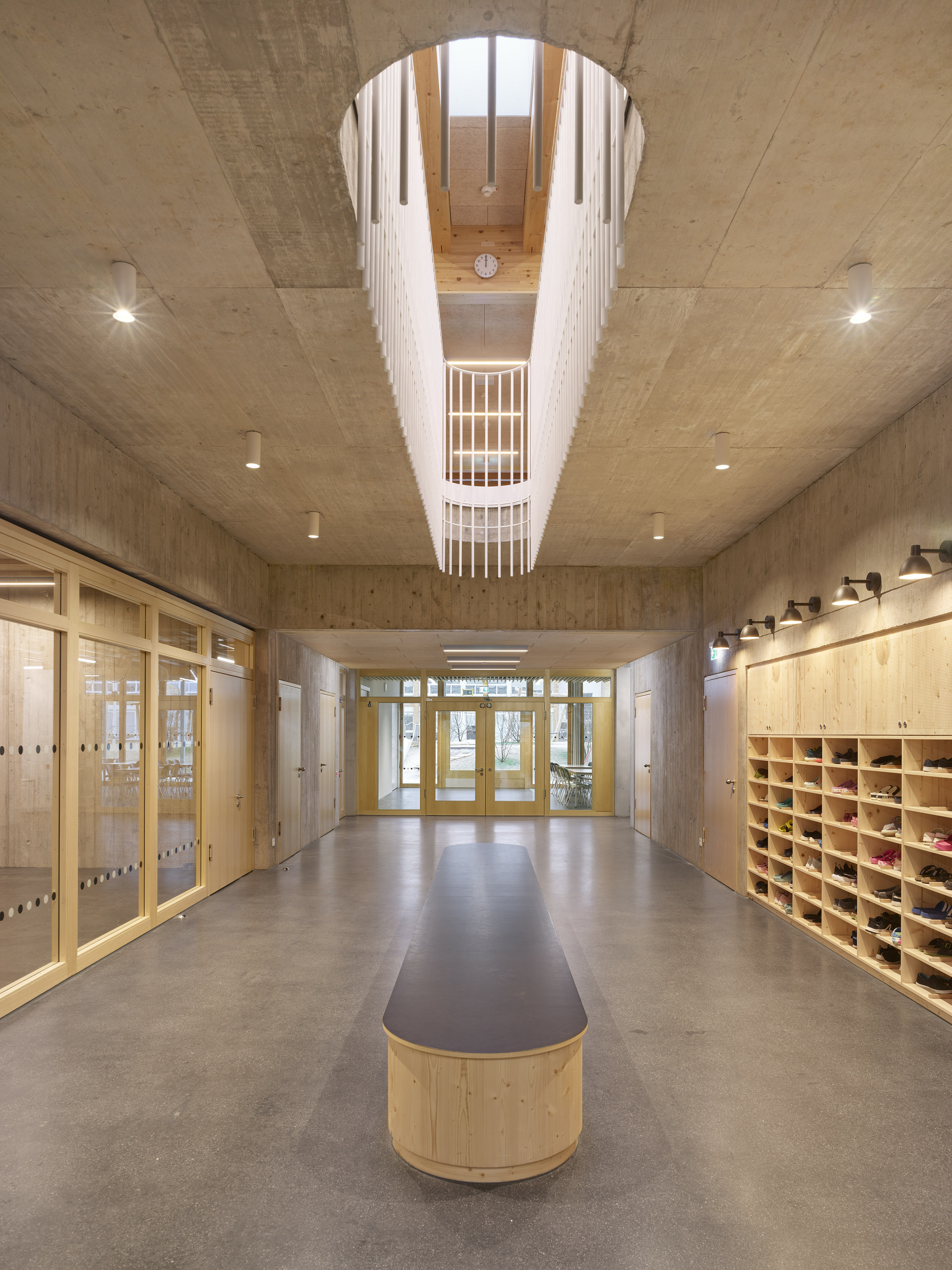 Entry corridor with cylindrical skylight above a curved bench under exposed concrete ceilings