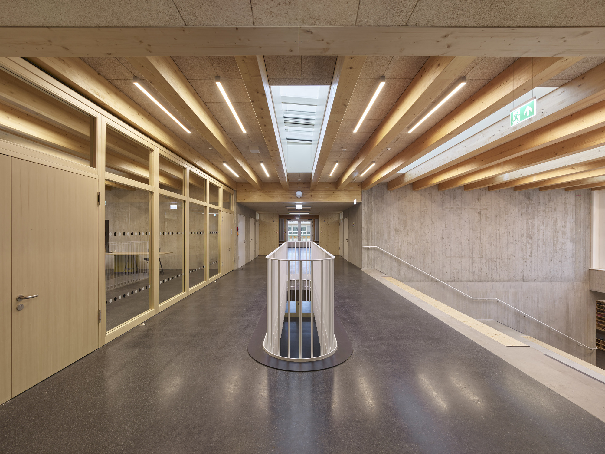 Corridor with exposed timber beams and cylindrical void beneath linear skylights and pendant lights