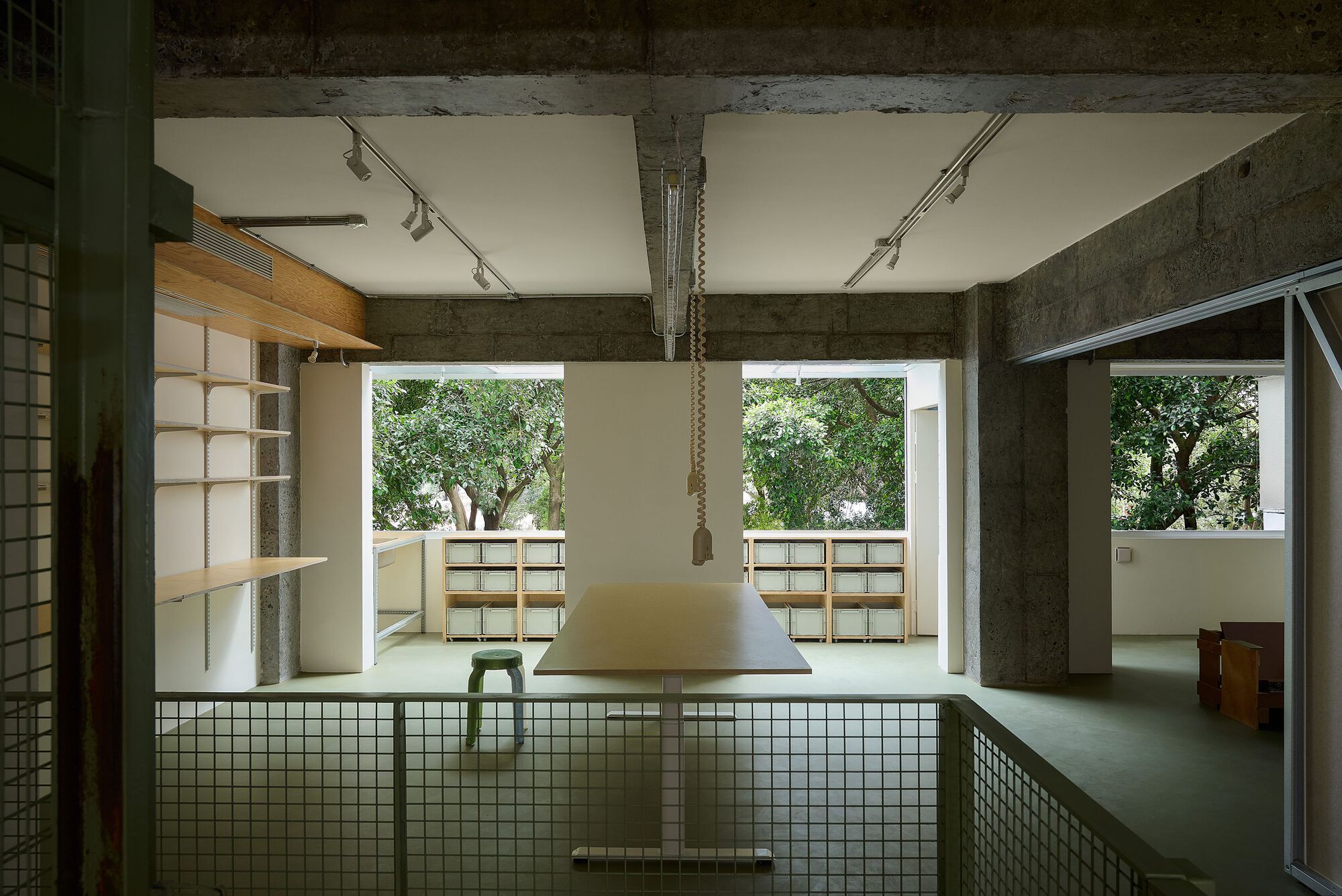 View across green mesh railing toward plywood storage units framed by concrete structure and trees beyond