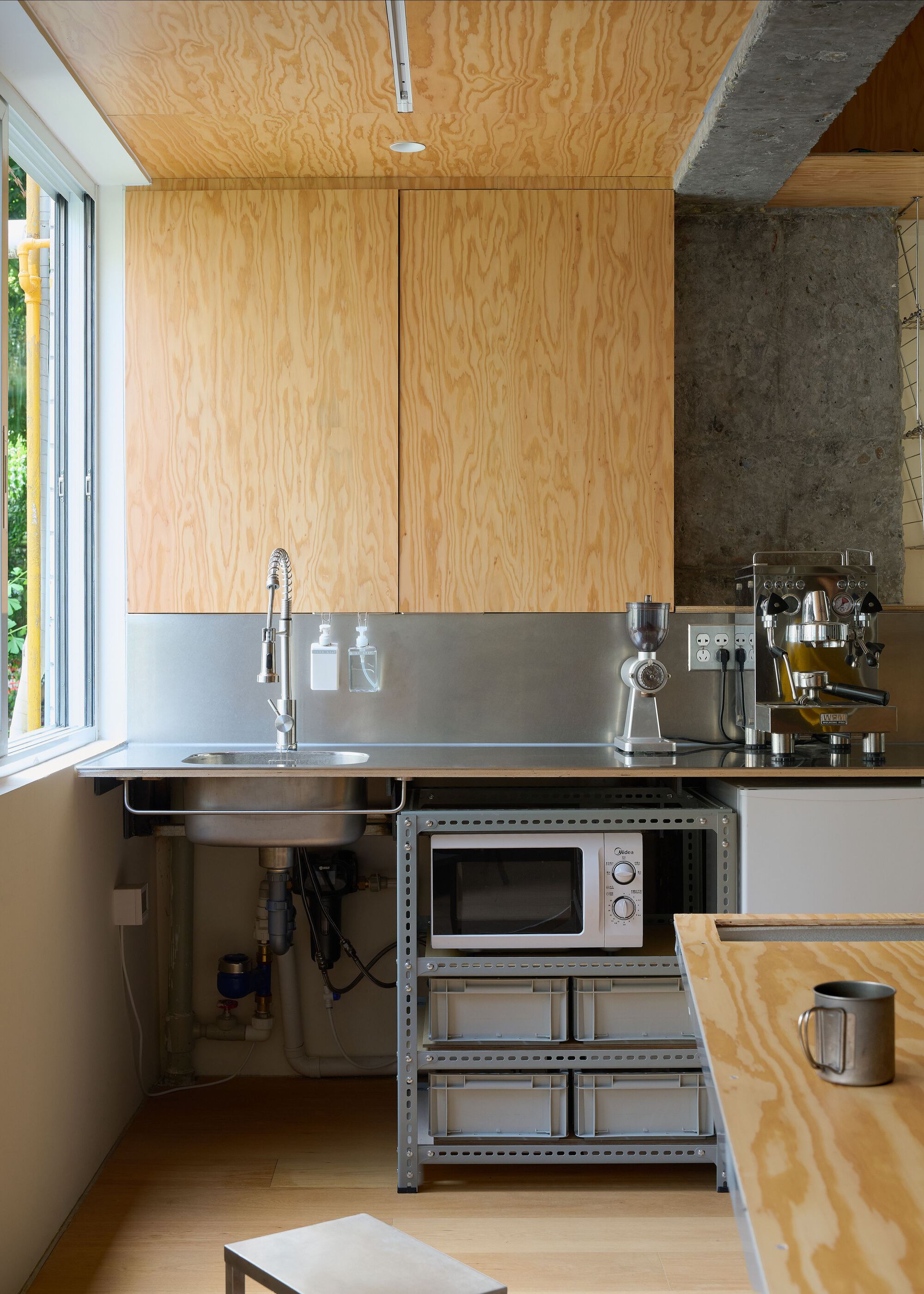 Compact kitchen with plywood cabinetry and ceiling above a stainless steel counter and sink