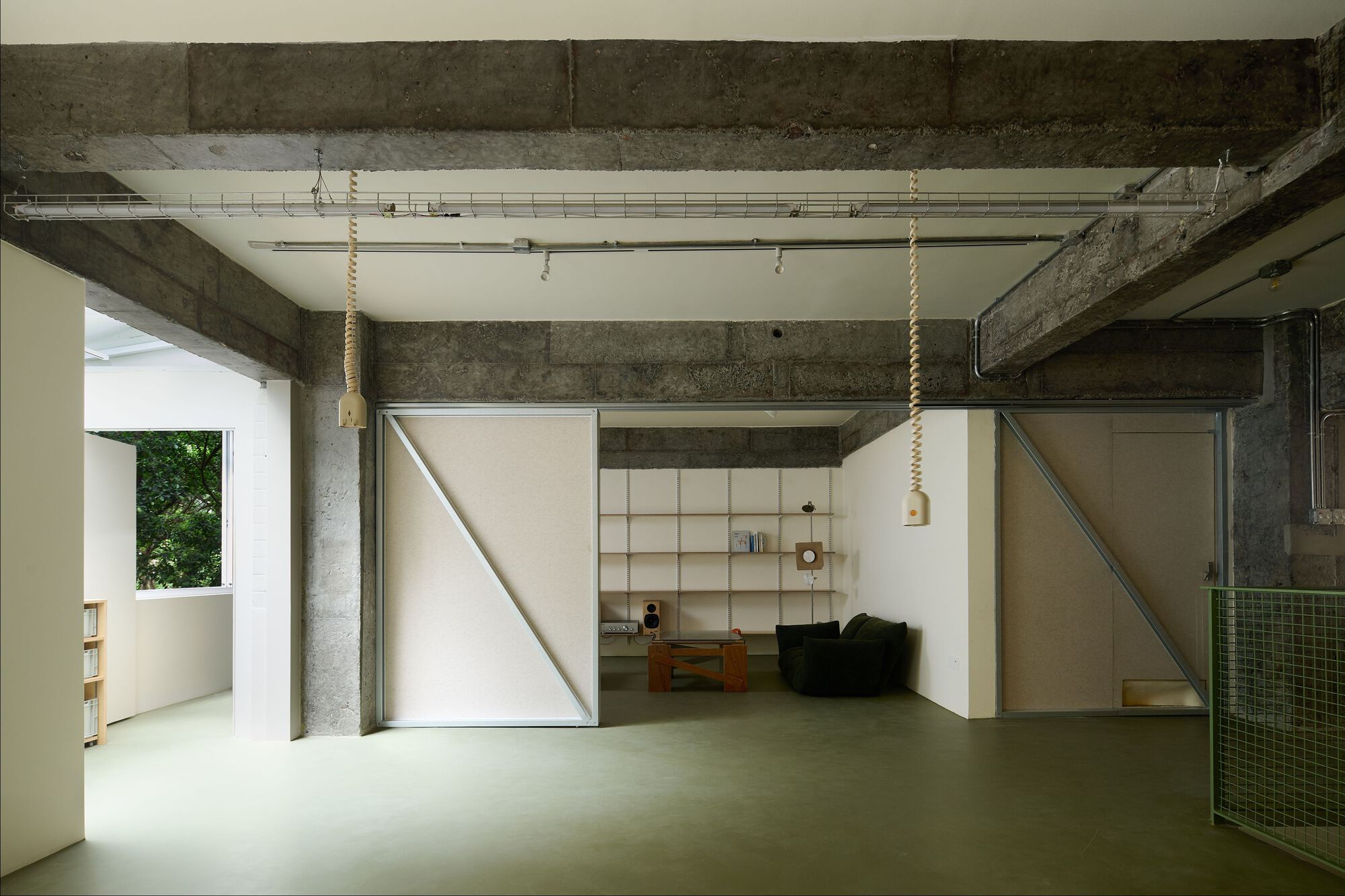Open interior with exposed concrete beams and pivoting white panel doors framing a workspace beyond