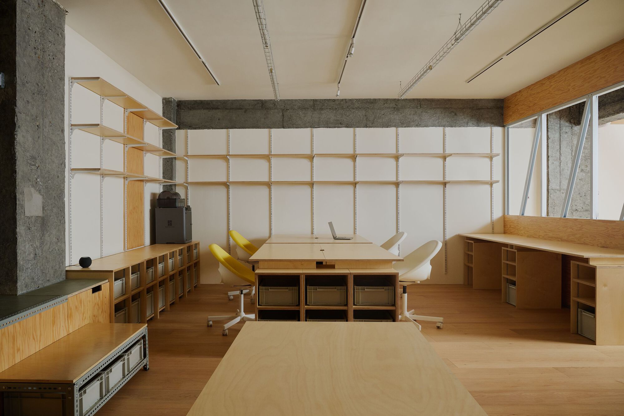 Workspace with plywood desk and shelving units beneath a timber and fabric grid wall system