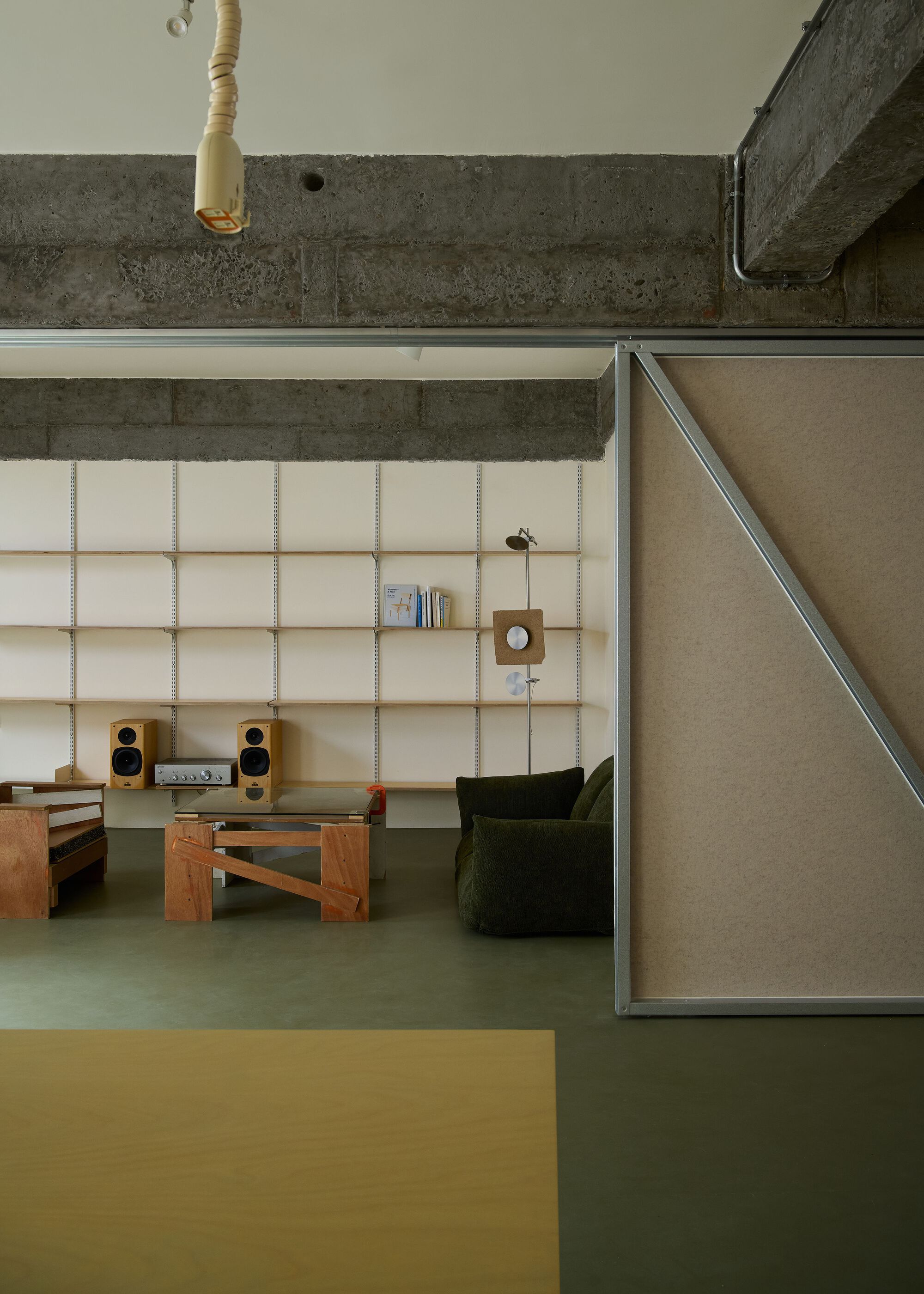 Corner detail showing pivoting fabric panel and timber shelving beneath raw concrete beams