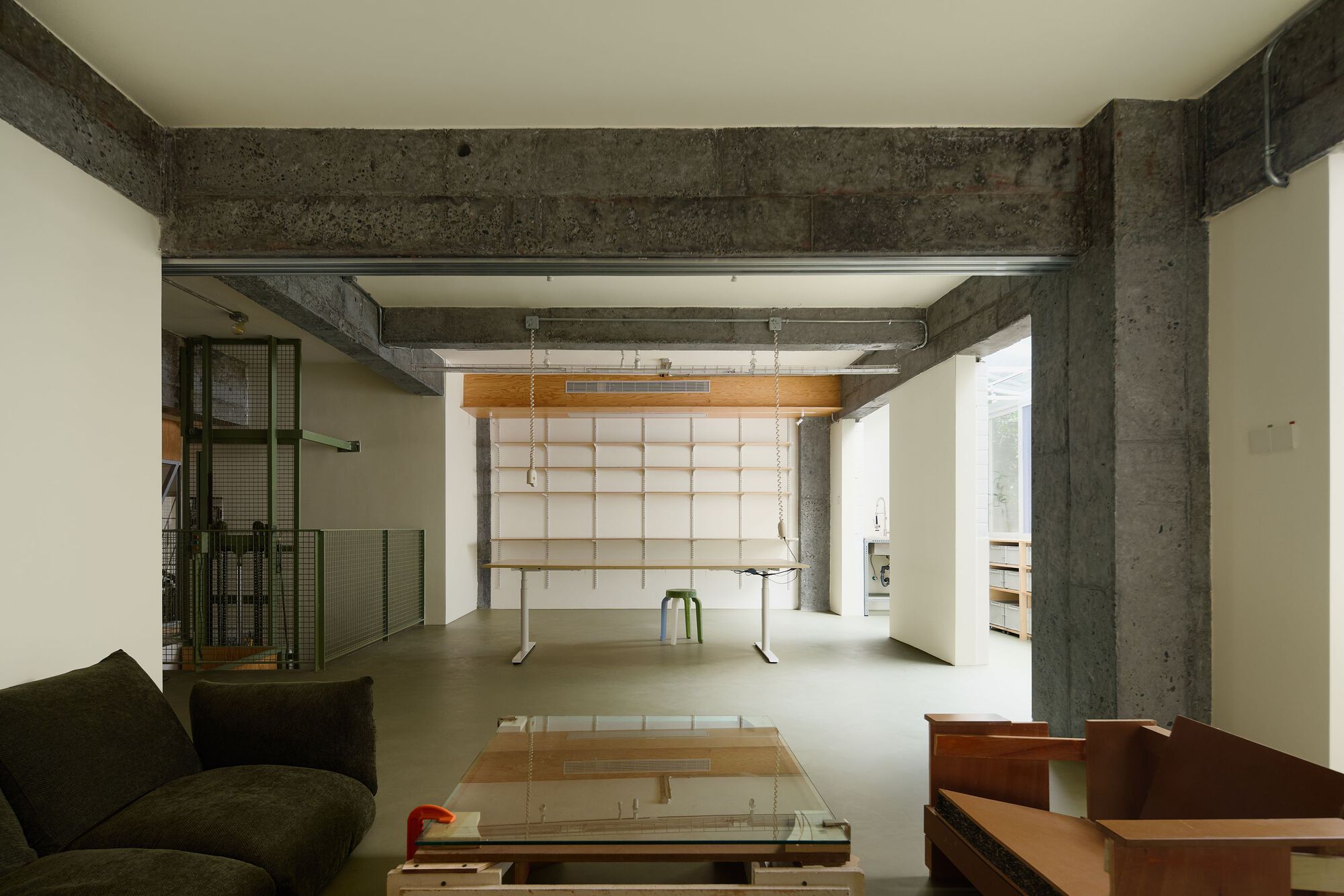 Living area with glass coffee table and gridded fabric wall beneath exposed concrete structural frame