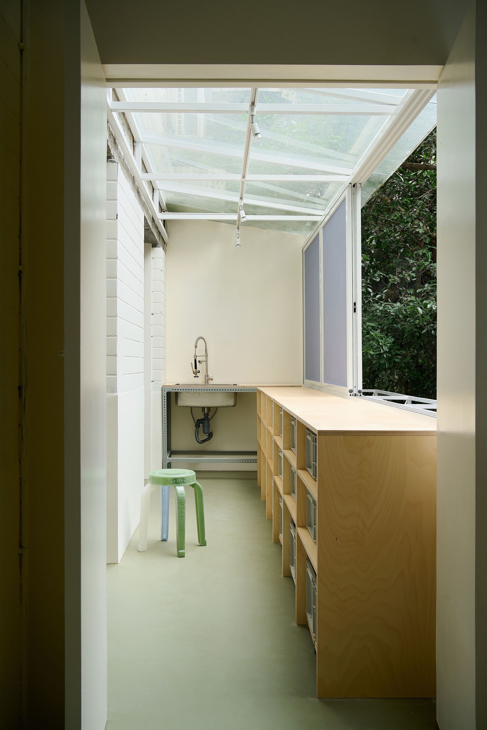 Workspace with glass skylight roof above timber counter and wall-mounted sink beside greenery