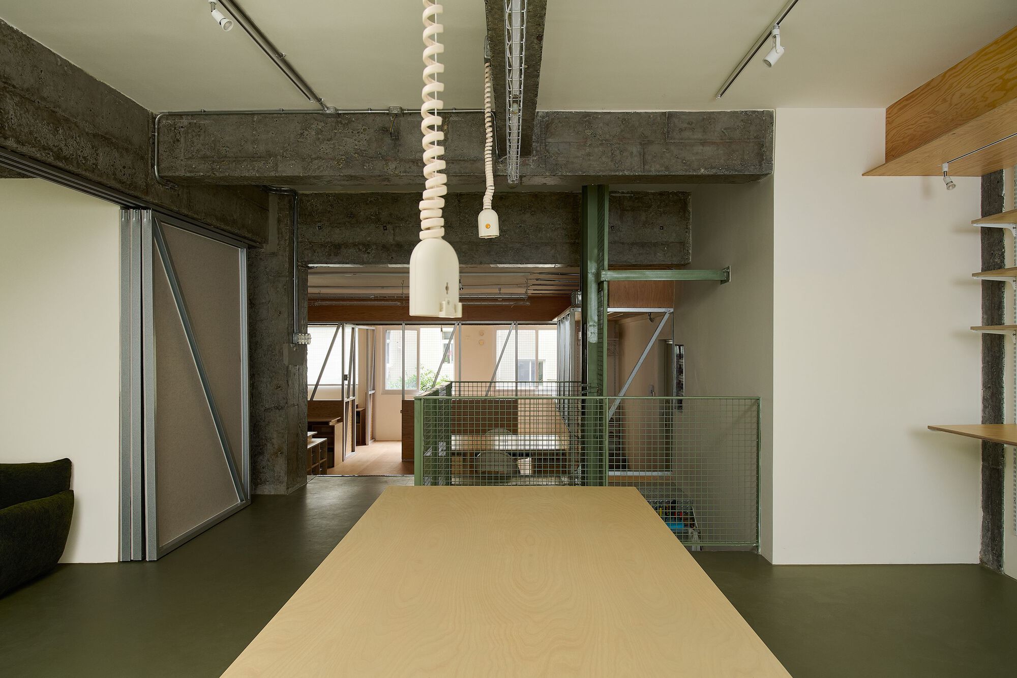 Long plywood table extending toward green mesh storage enclosure under exposed ceiling ducts and concrete beams
