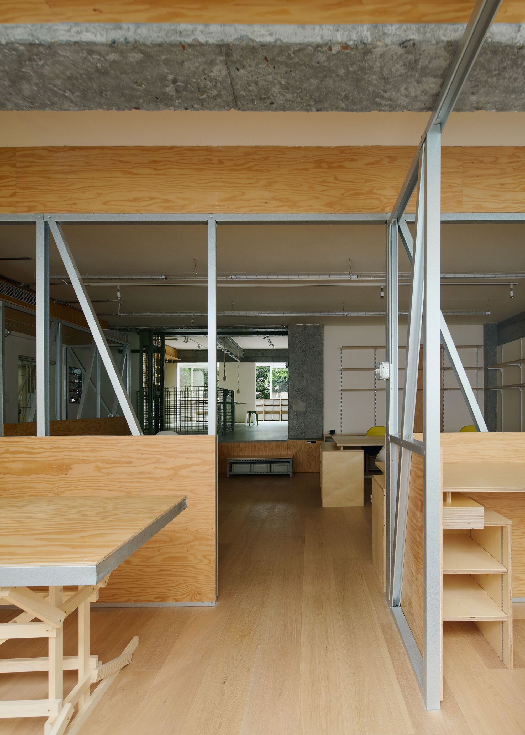 Interior workspace with steel bracing frames, plywood ceiling panels and raised plywood platforms under exposed concrete beams