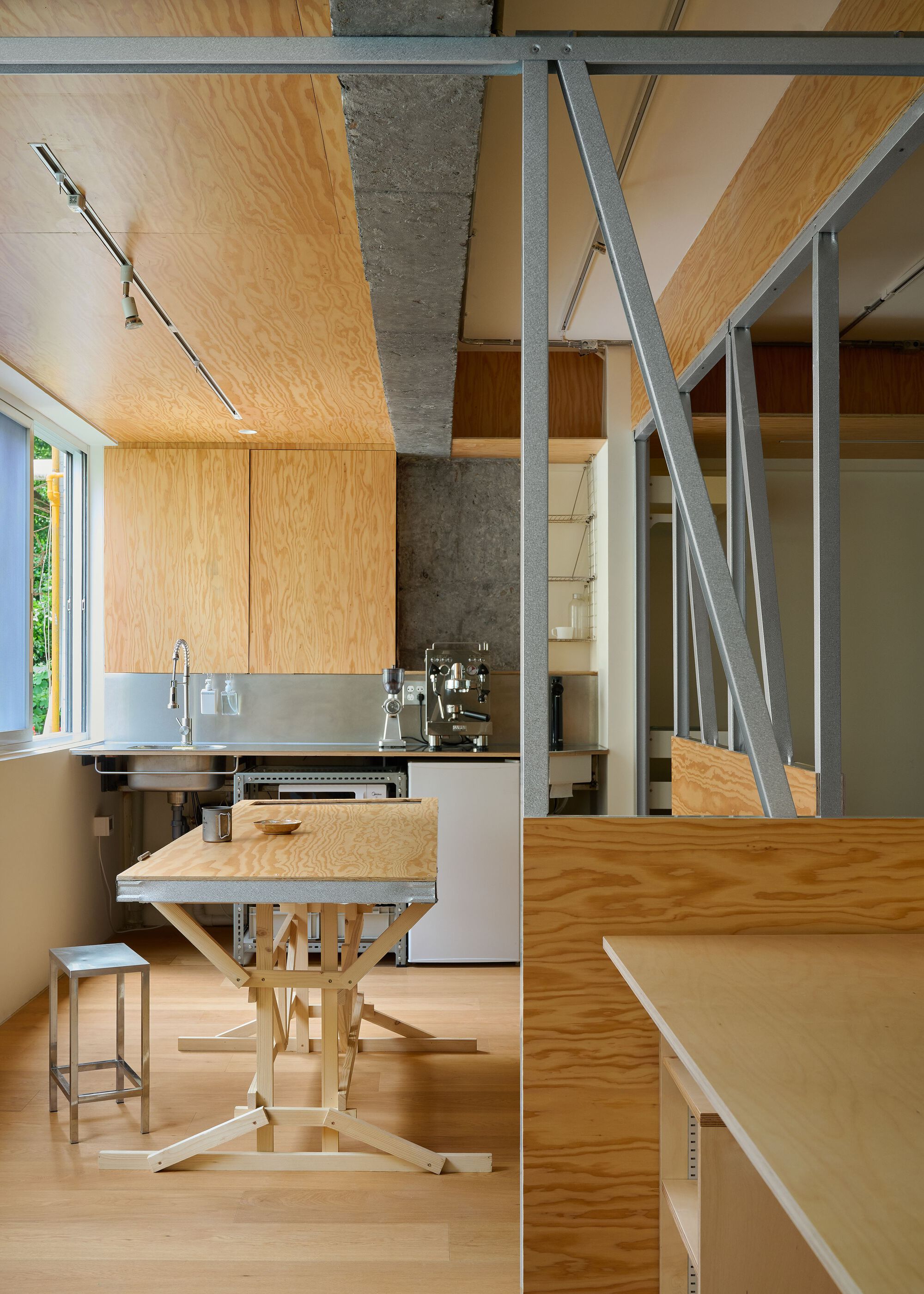 Kitchen counter with stainless sink beside a plywood height-adjustable table and steel diagonal bracing