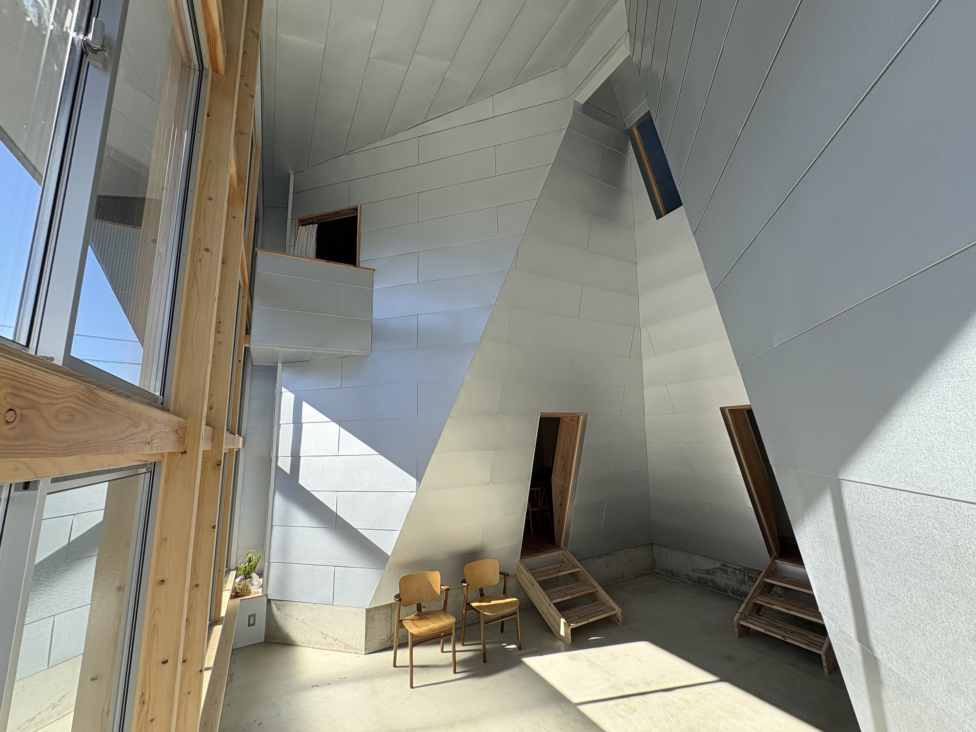 Double-height interior space with angled white panel walls and timber framed openings in bright daylight