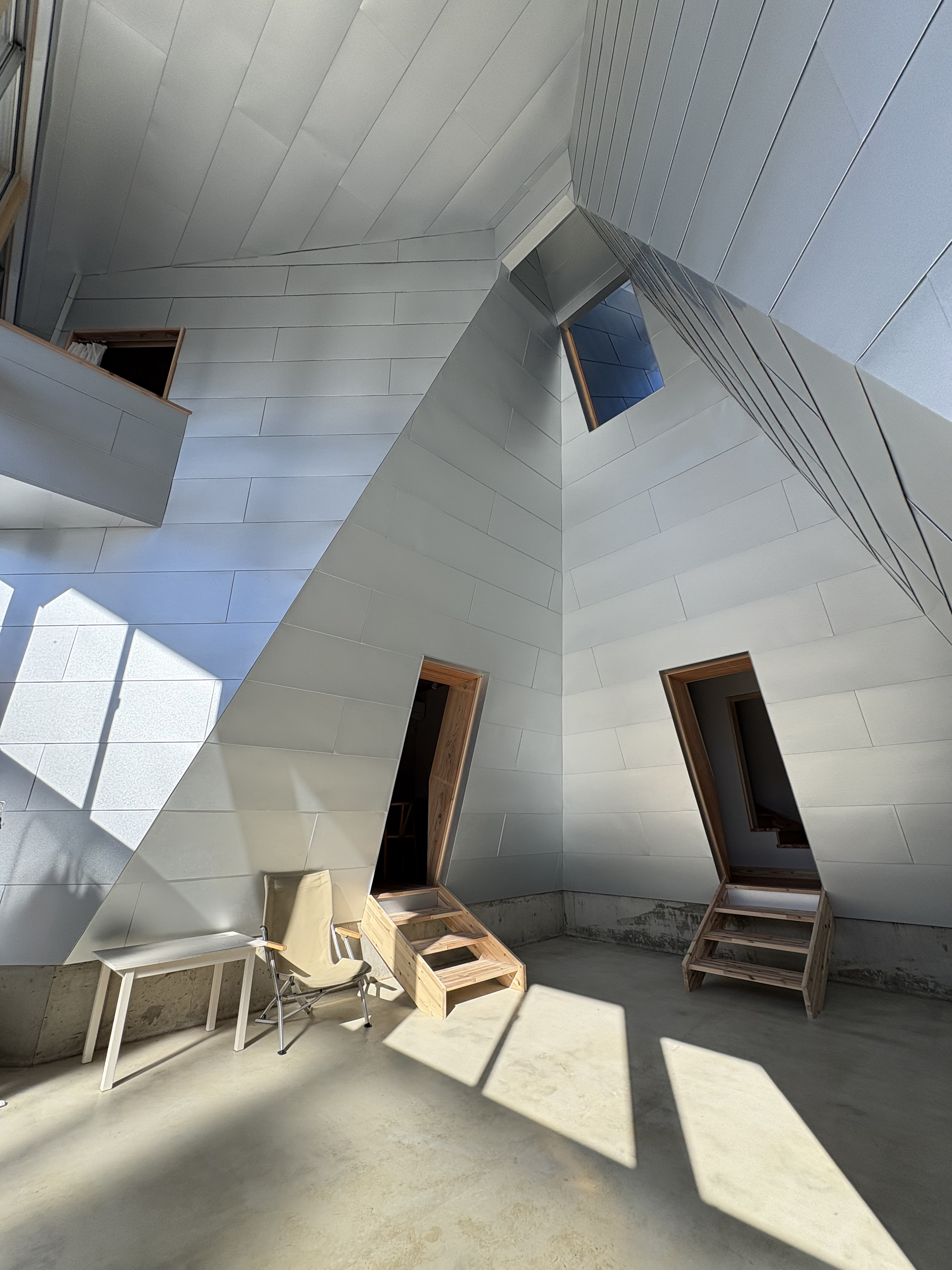 View of the faceted white panel ceiling and timber doorways casting sharp shadows on concrete floor