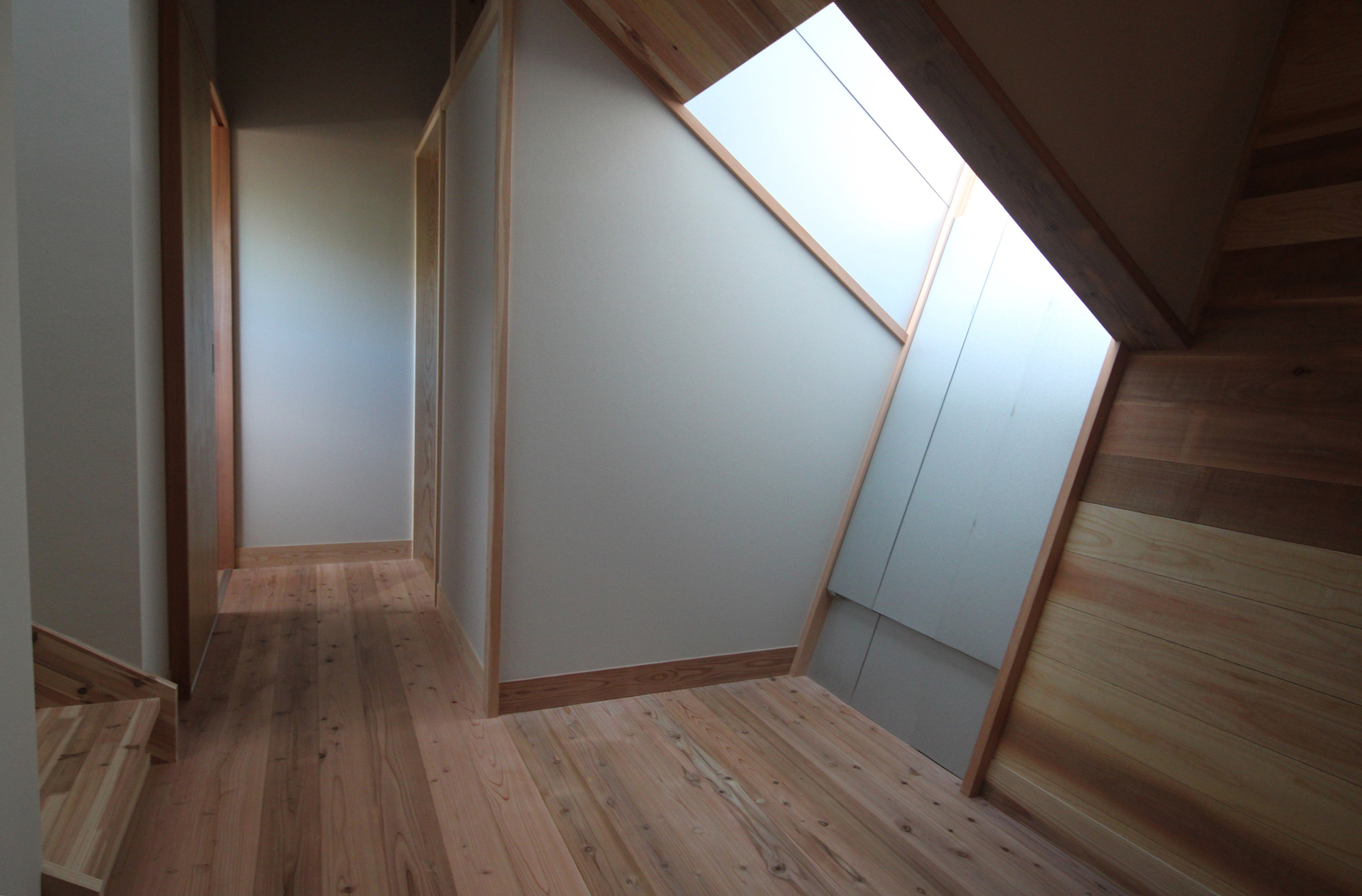 Upper hallway with angled skylight framed in timber and white painted walls meeting wood flooring