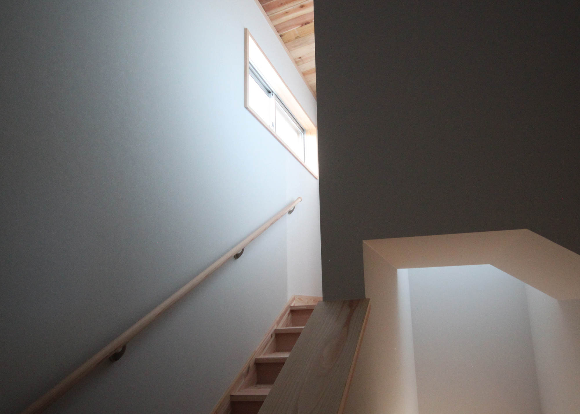 Timber stair with simple handrail ascending toward a high window in white plaster walls