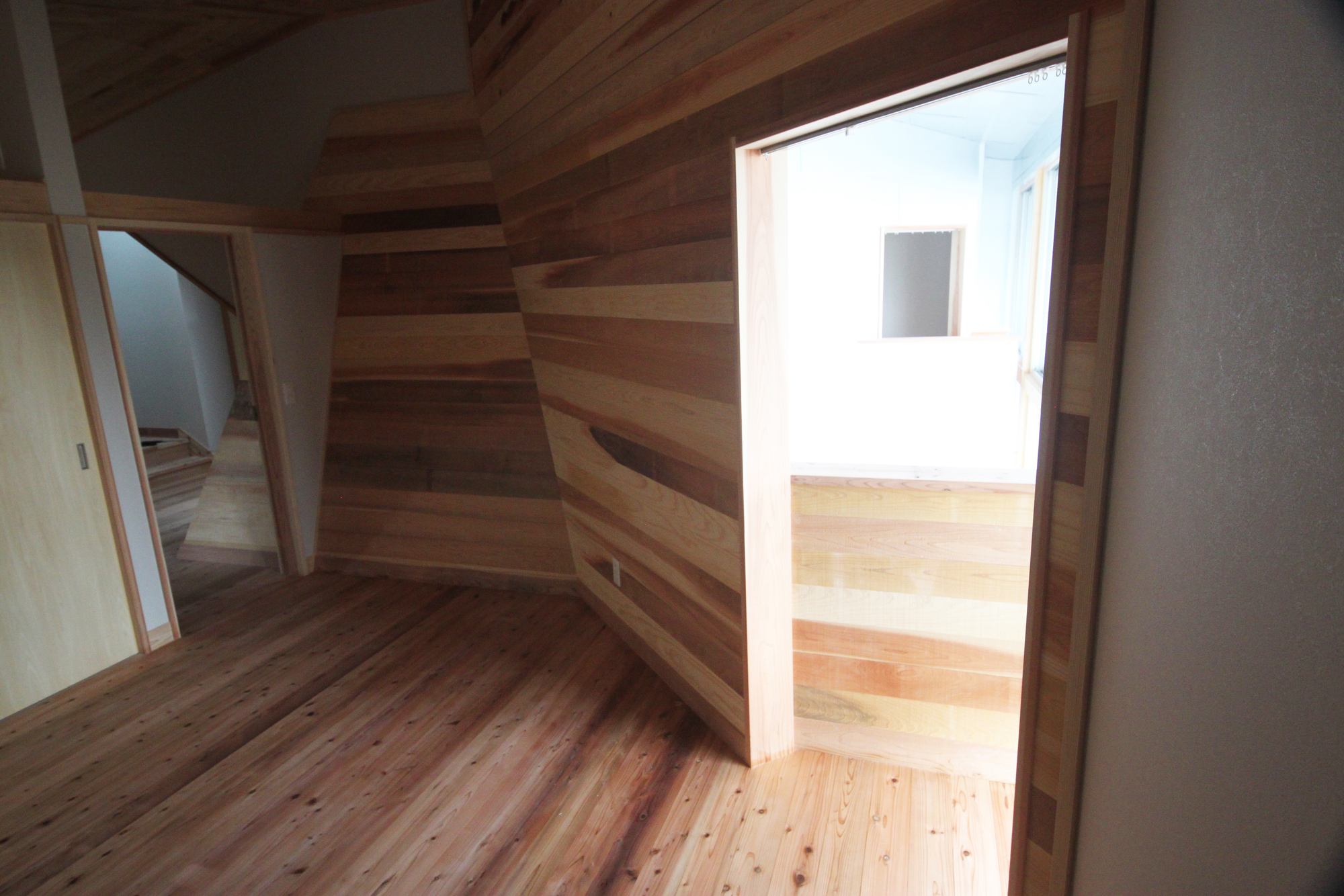 Corner room with horizontal timber plank walls and doorway opening to an adjacent sunlit space