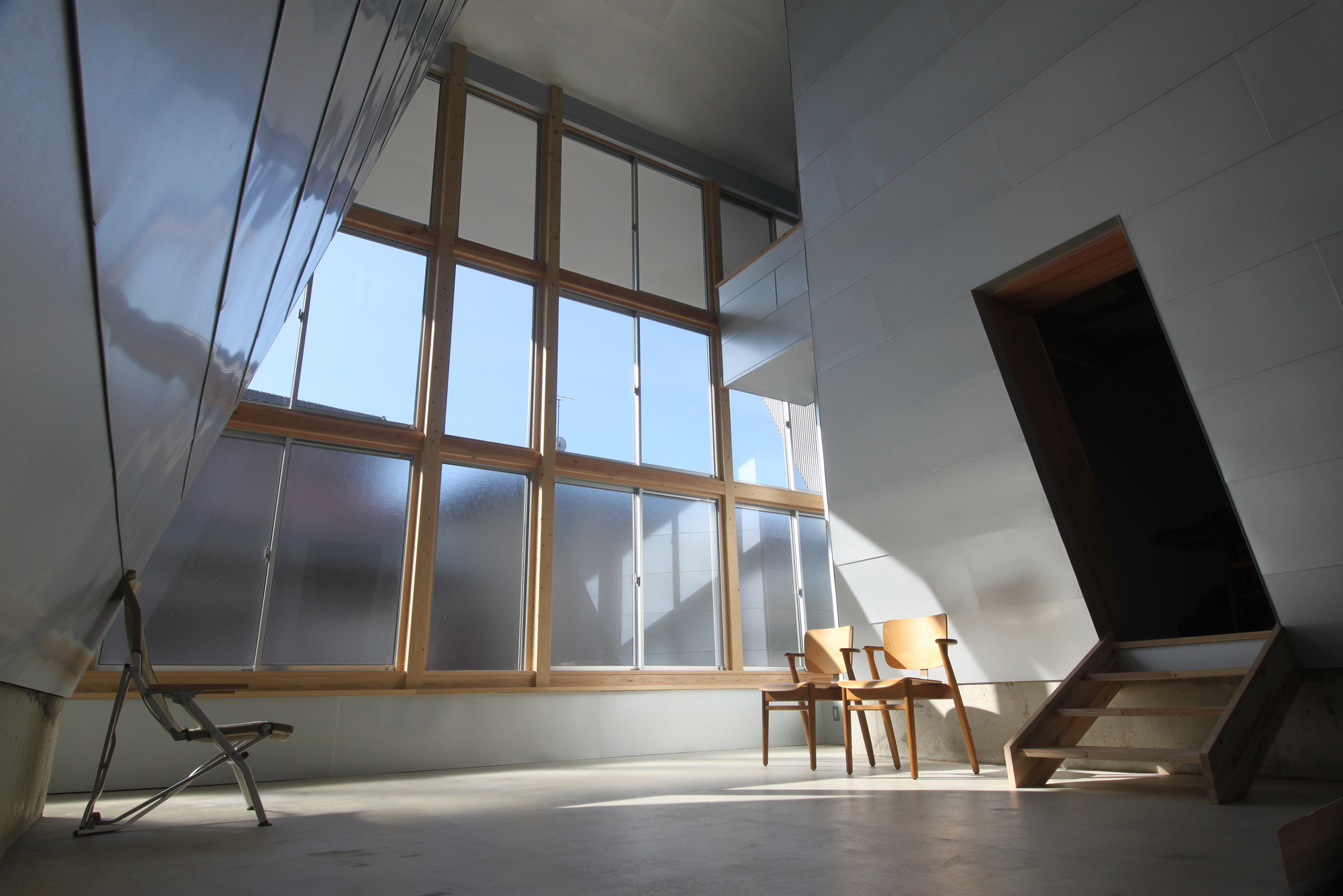 Double-height interior space with timber-framed window wall and angled ceiling planes under bright daylight