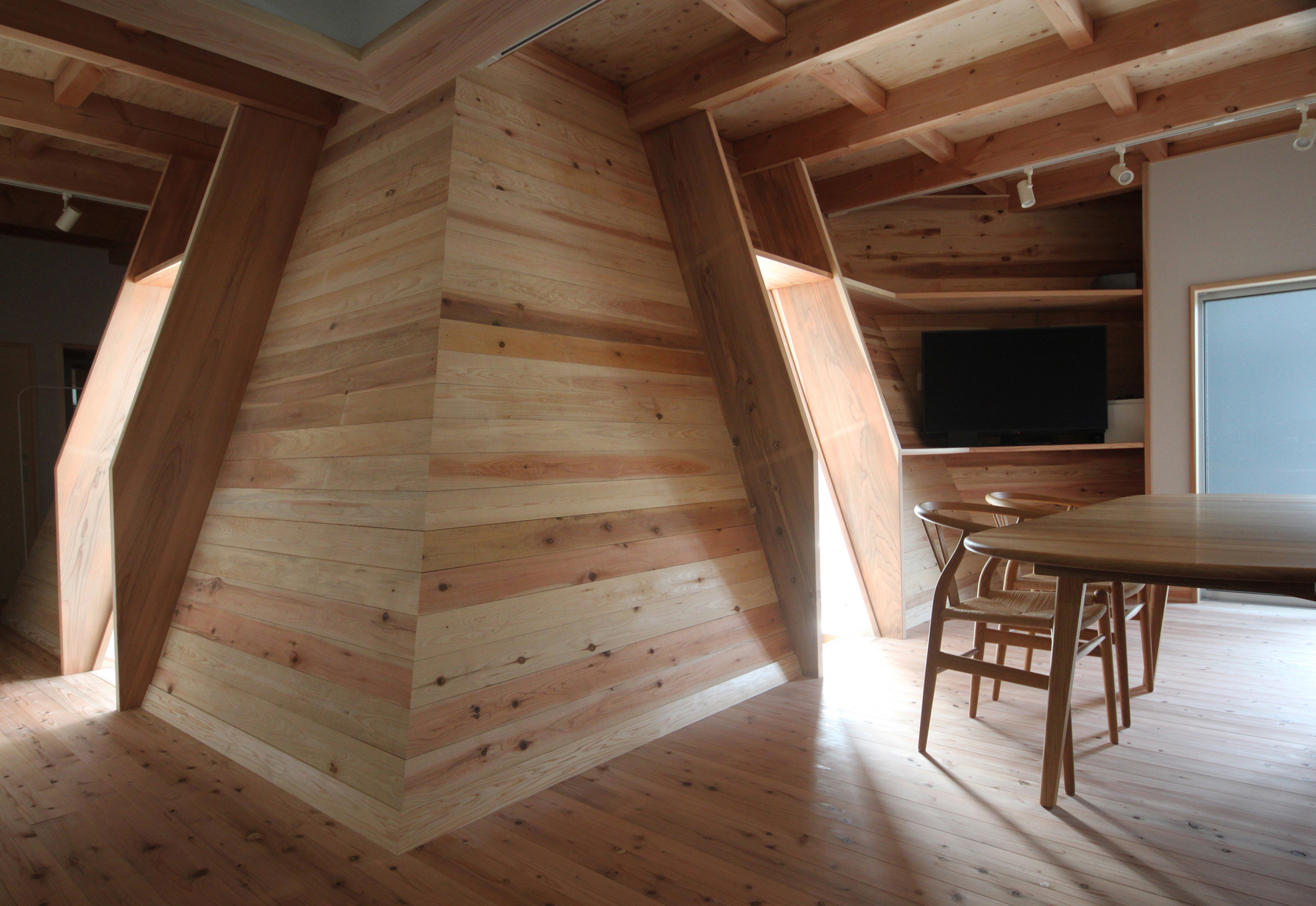 Angled timber-clad wall meeting exposed beam ceiling and dining area with track lighting overhead