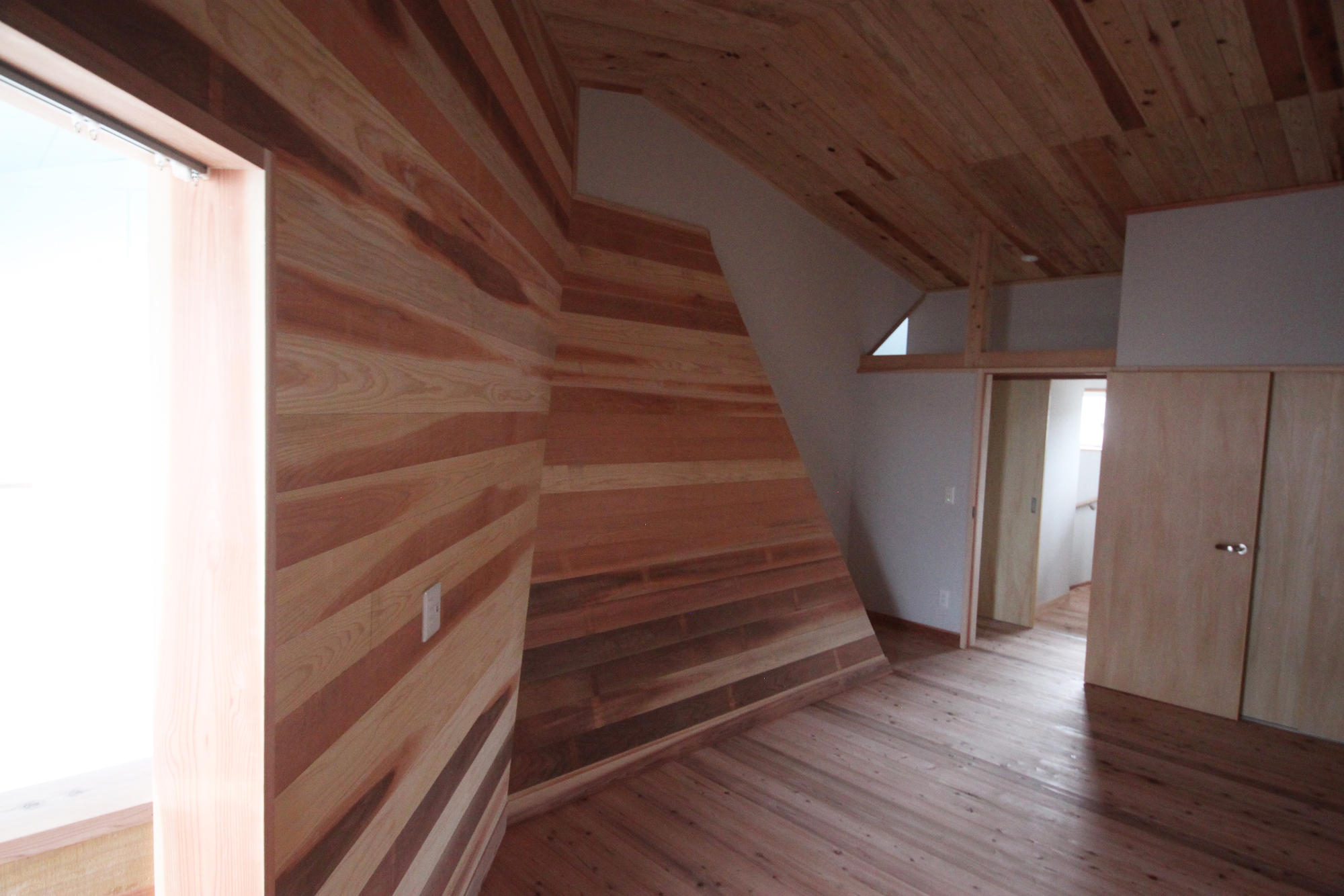 Sloped timber wall with horizontal planking under exposed wood beam ceiling in upper level corridor