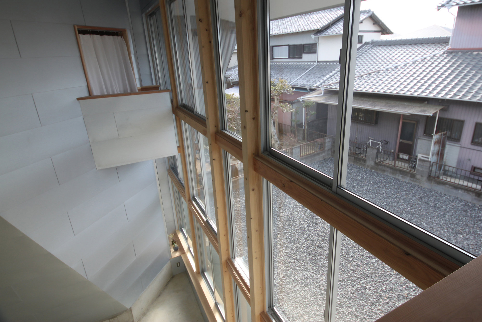 Angled timber-framed window wall overlooking gravel courtyard and neighboring tile-roofed houses