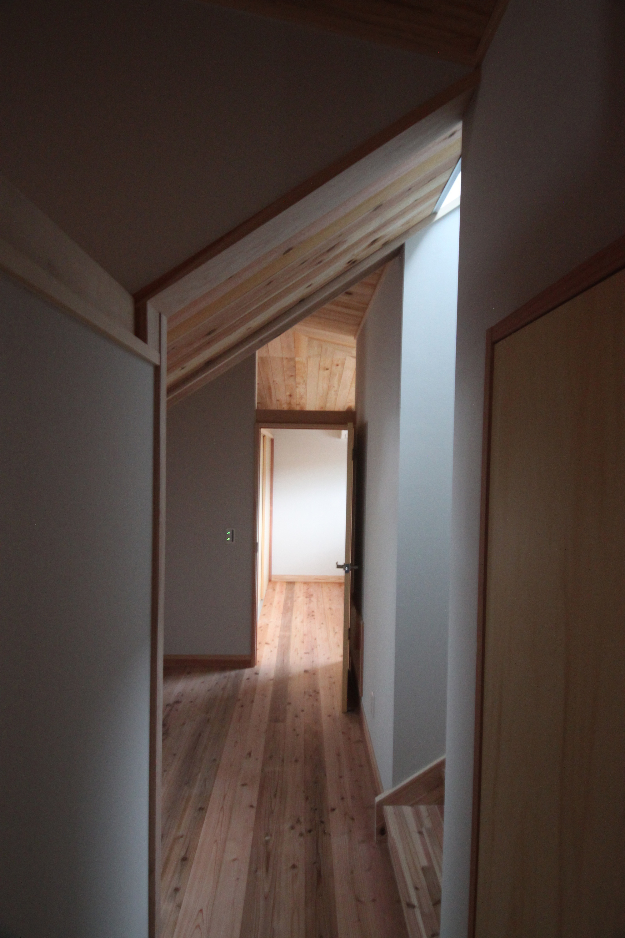 Interior hallway with pale wood flooring leading through white walls to a softly lit room beyond