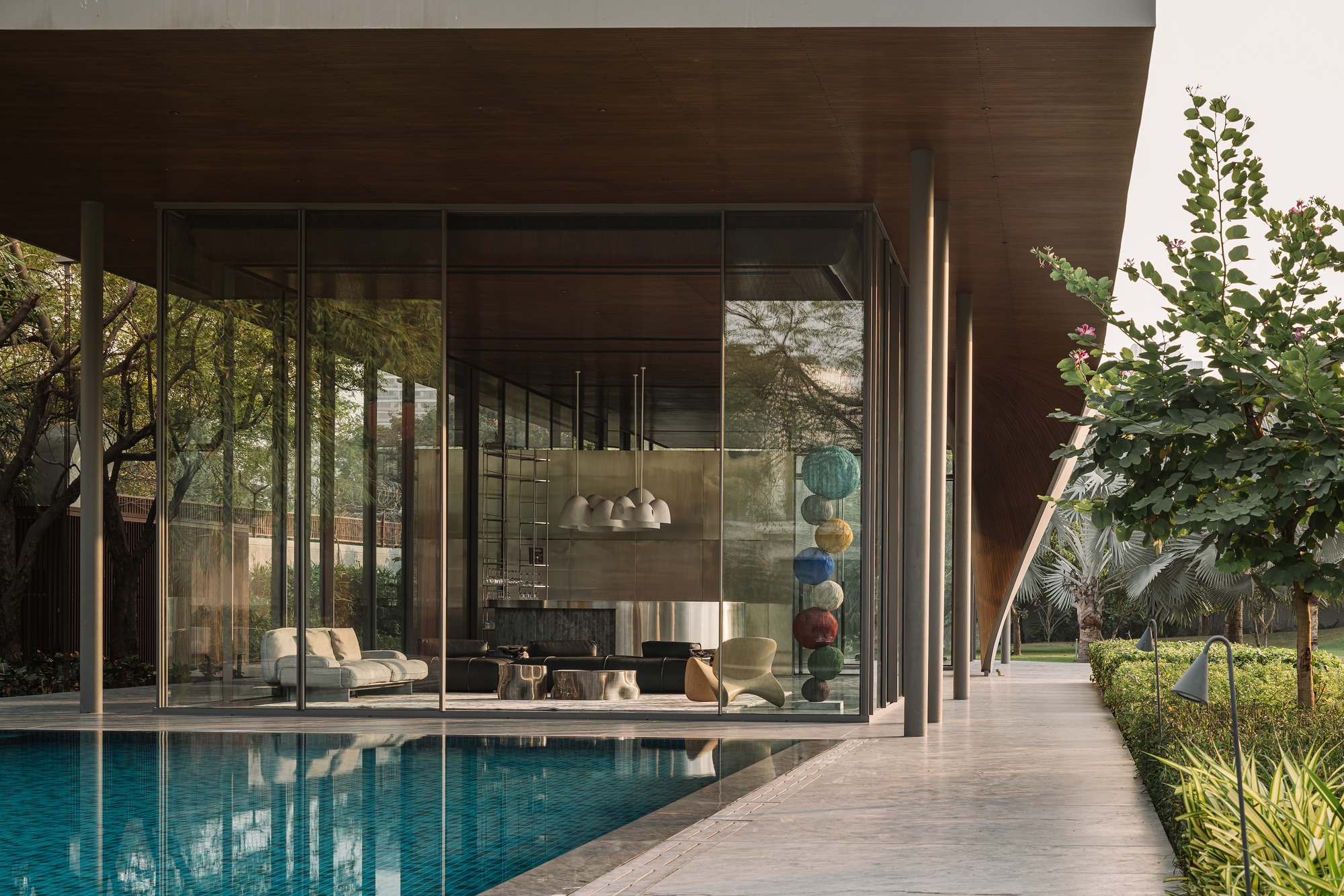 Poolside terrace with floor-to-ceiling glass walls reflecting the water and surrounding plantings