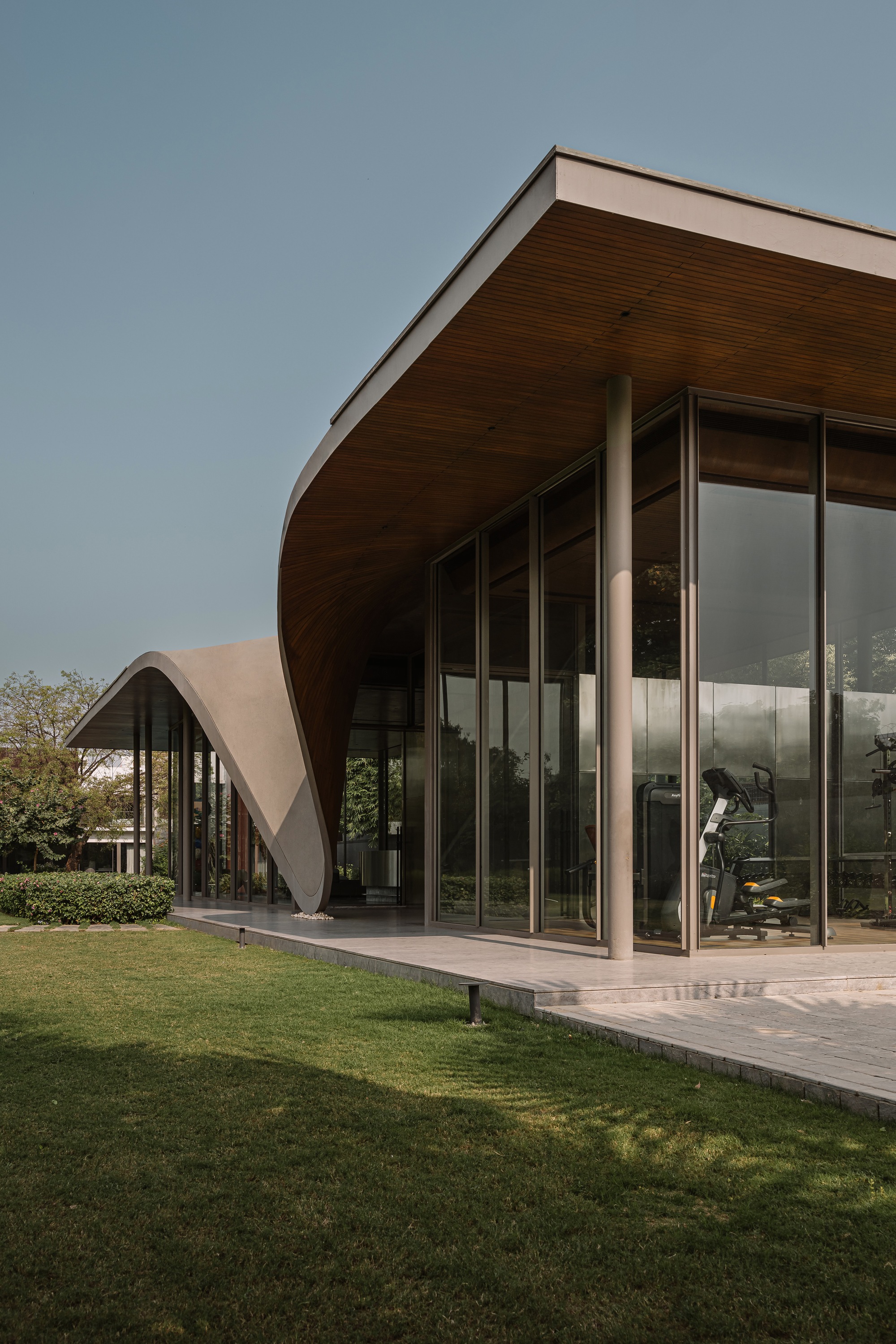 Curved roof edge with timber soffit sweeping over floor-to-ceiling glass walls and lawn terrace