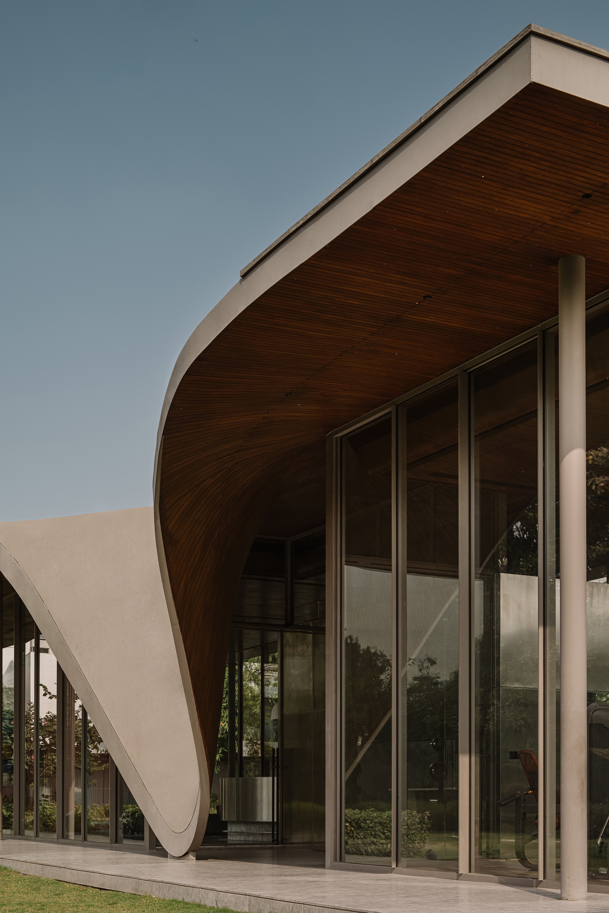 Close-up of the sculptural roof overhang with timber soffit meeting glass curtain wall below