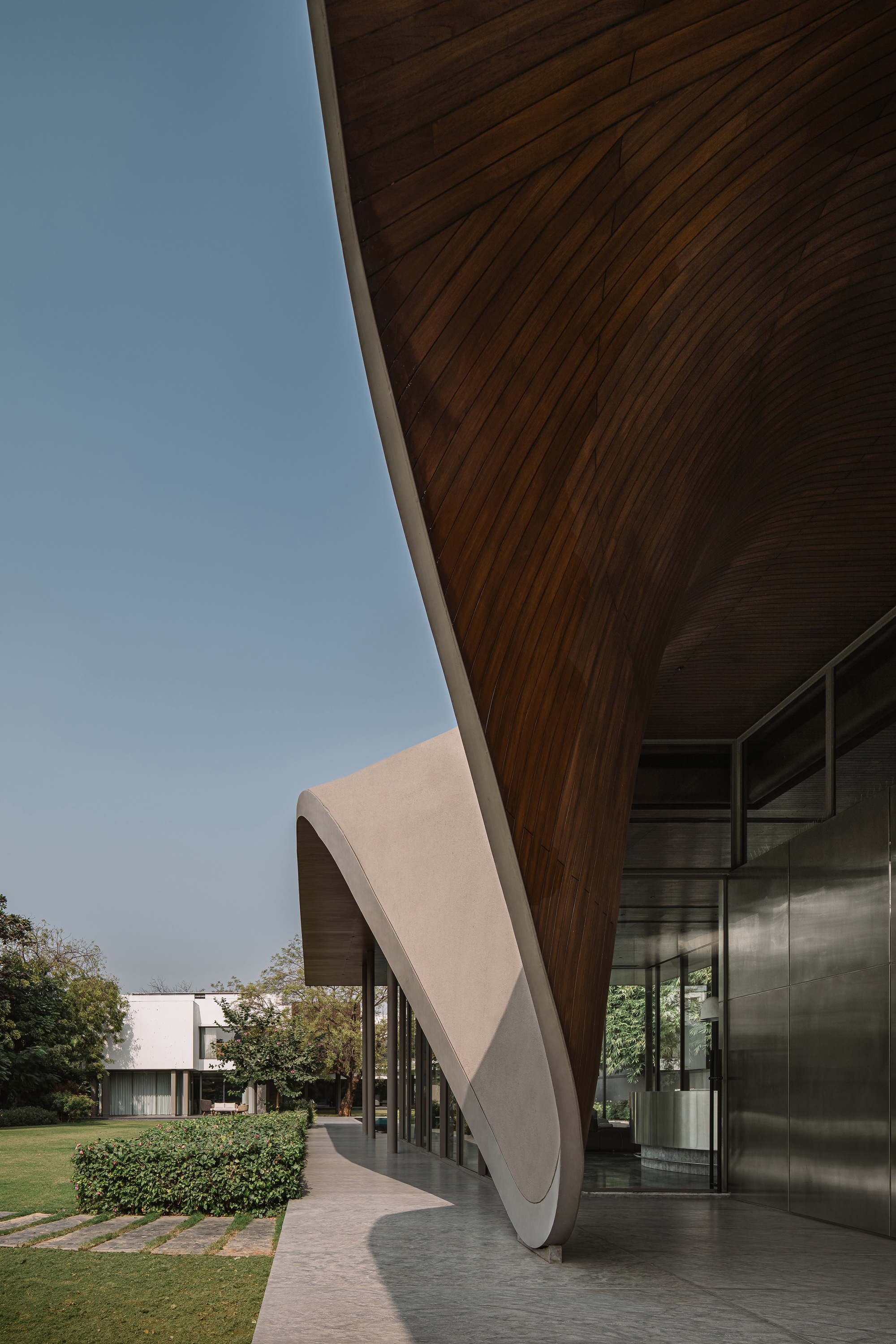 View along the underside of the curving timber roof canopy extending toward adjacent lawn and hedges
